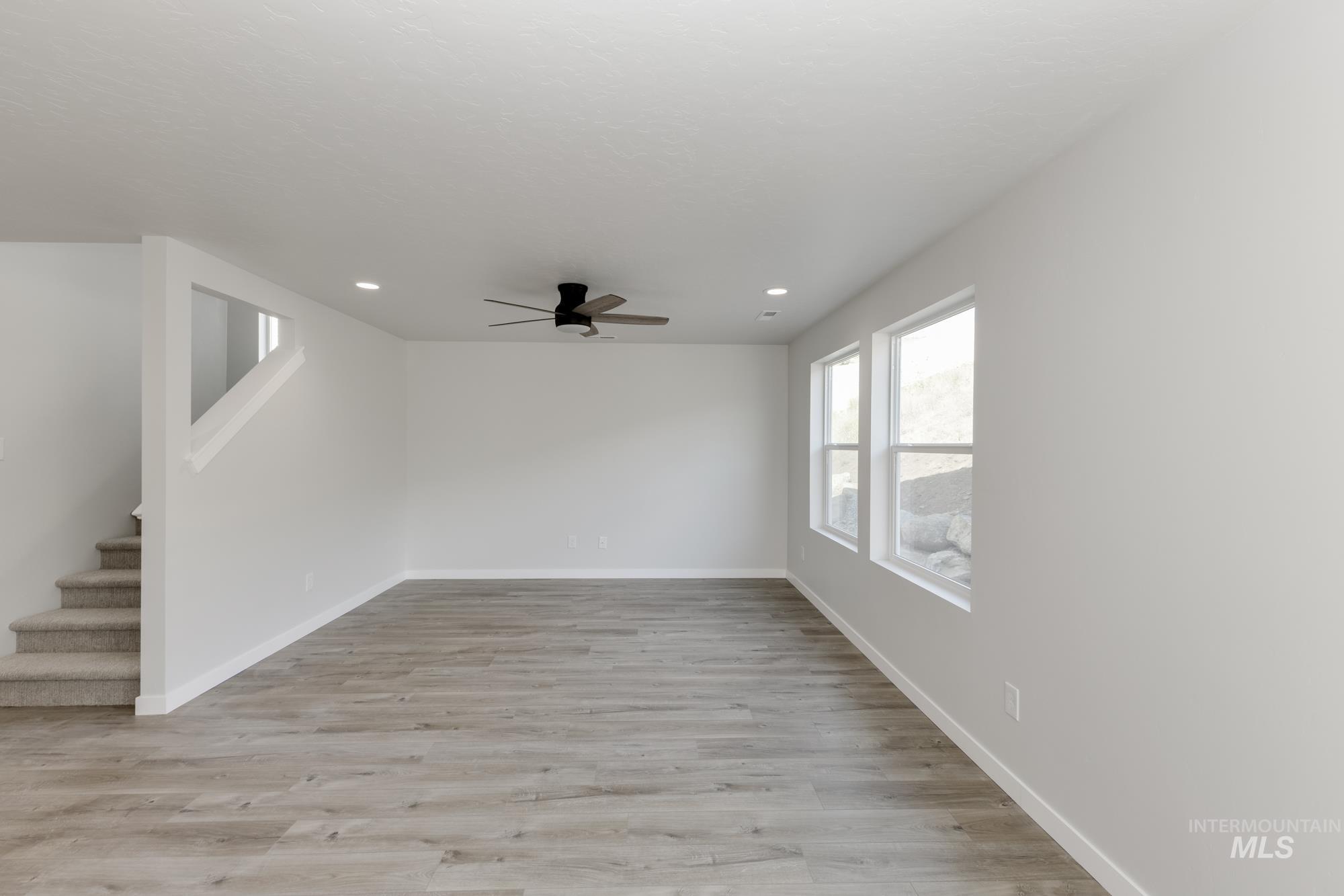 Spare room featuring light wood-style flooring, ceiling fan, recessed lighting, and stairway