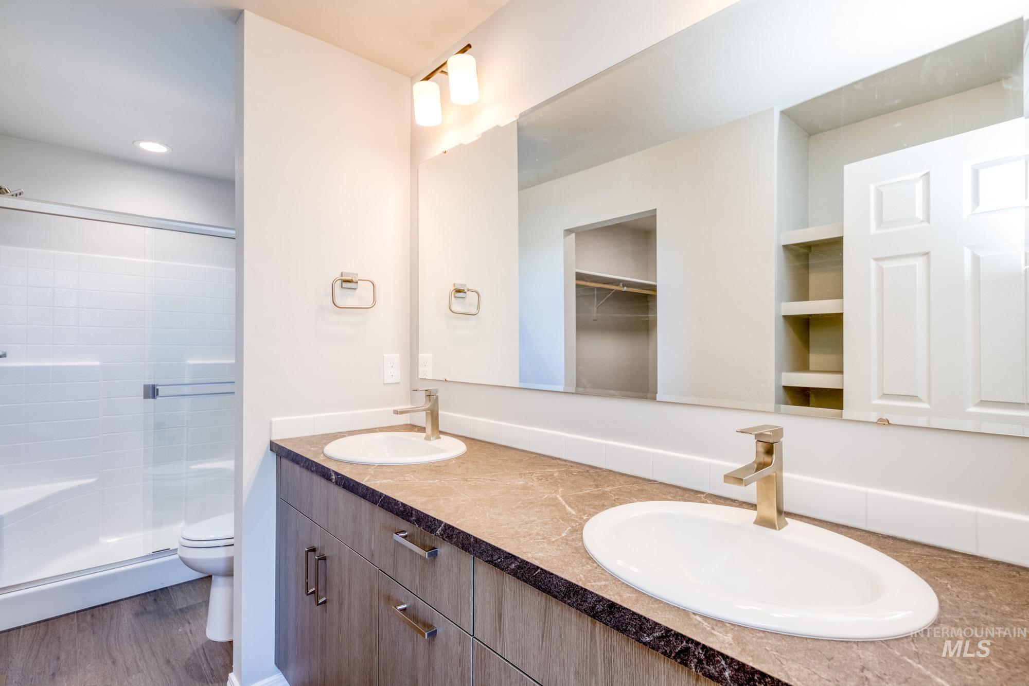 Bathroom with double vanity, dark wood-style floors, a shower stall, and a walk in closet