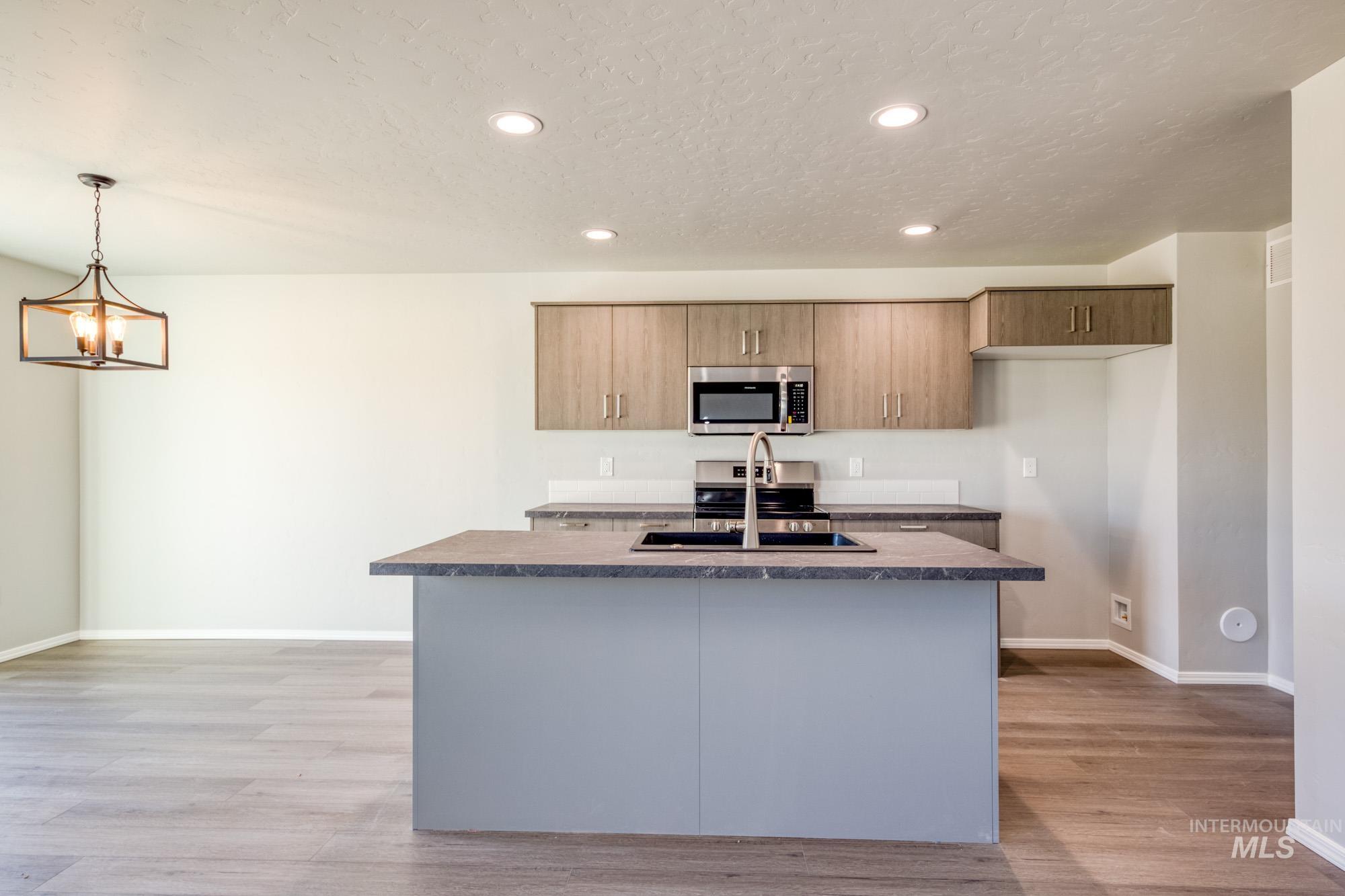 Kitchen featuring recessed lighting, stainless steel appliances, light wood-style flooring, a center island with sink, and decorative light fixtures
