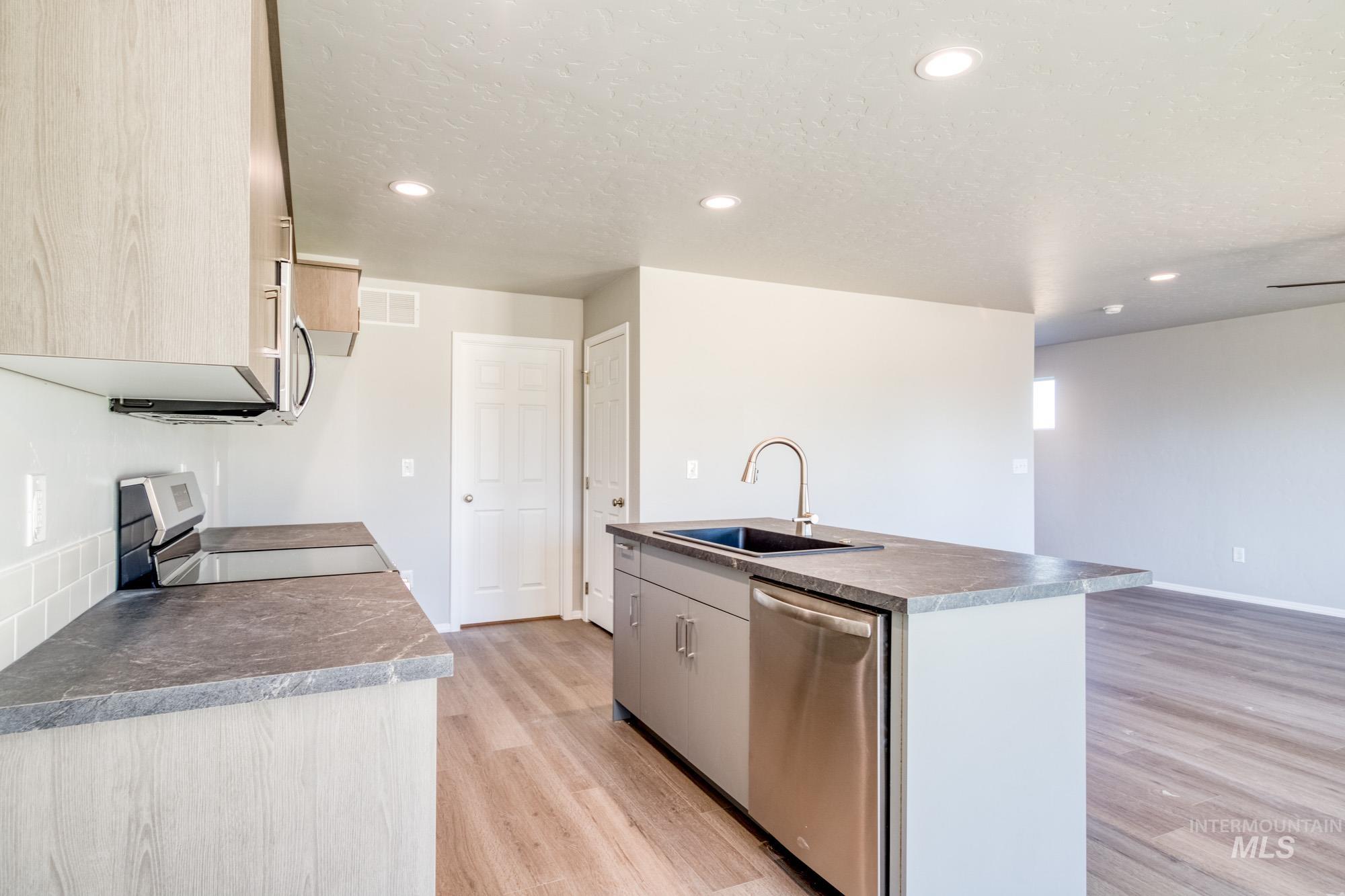 Kitchen with appliances with stainless steel finishes, recessed lighting, a kitchen island with sink, light wood finished floors, and dark countertops
