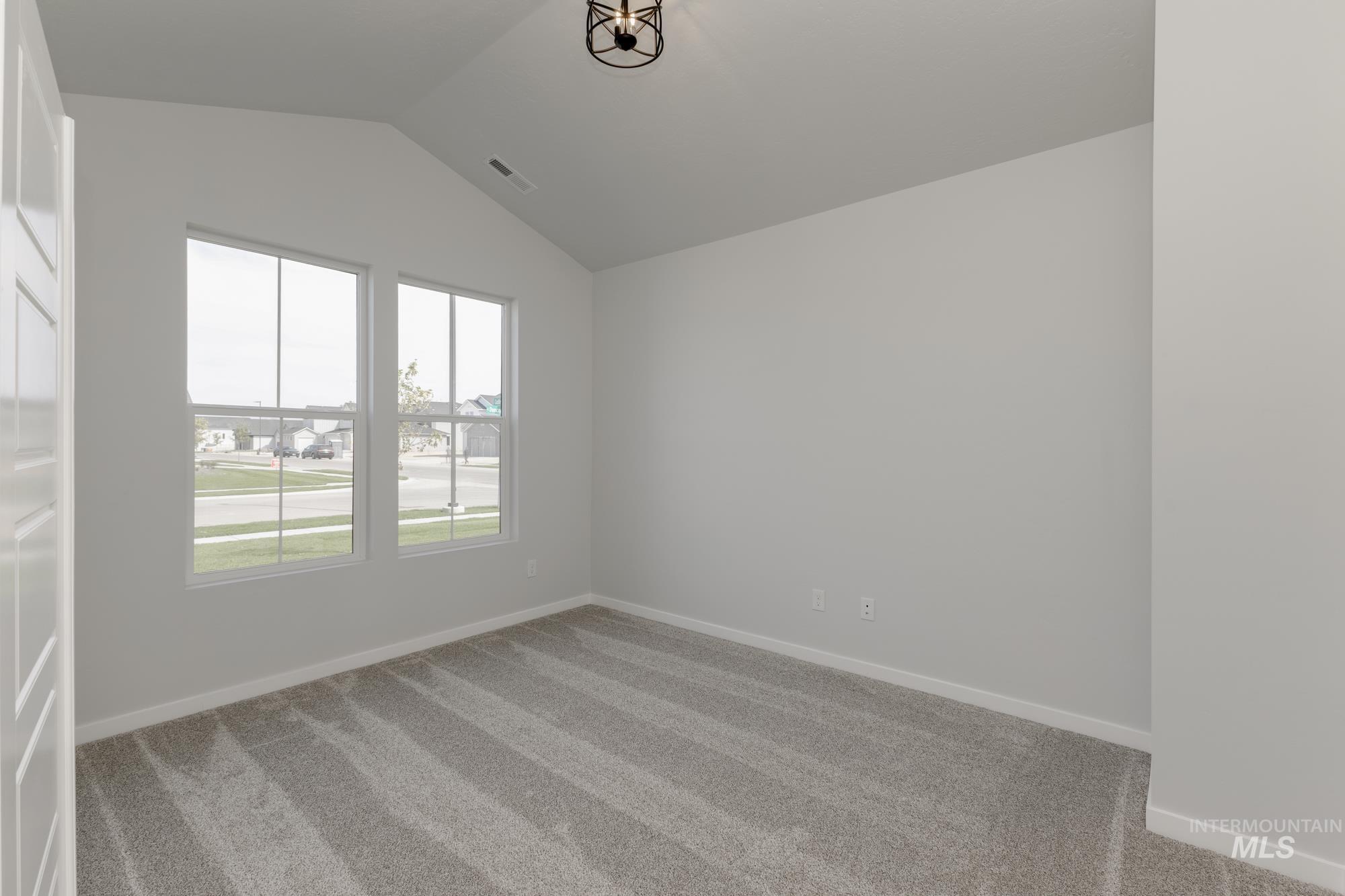Carpeted spare room featuring baseboards and lofted ceiling