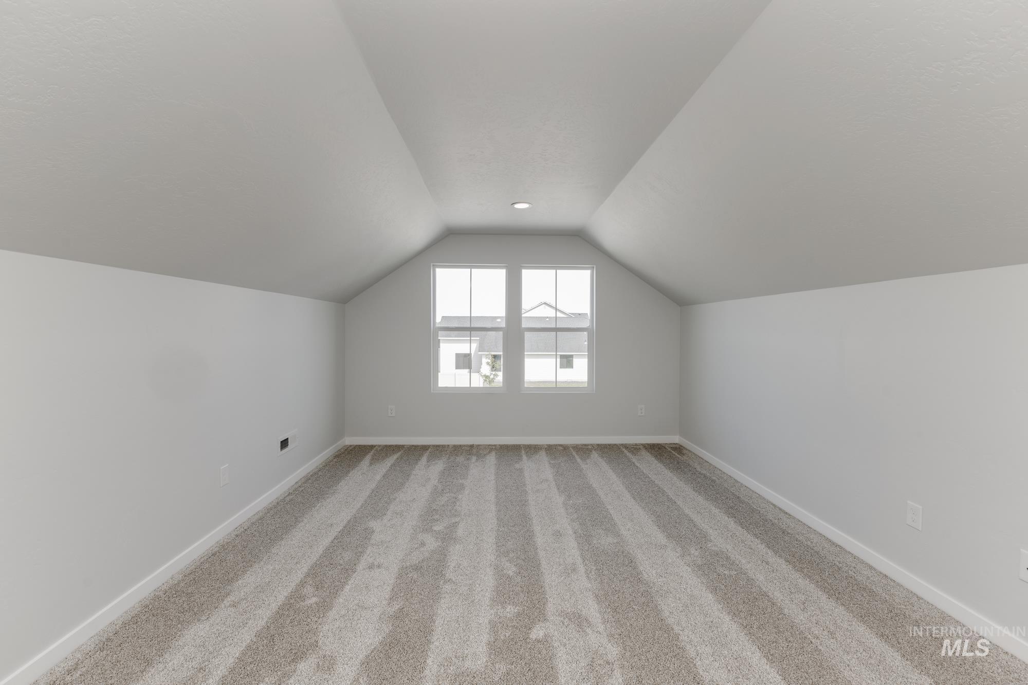 Additional living space featuring light colored carpet and lofted ceiling
