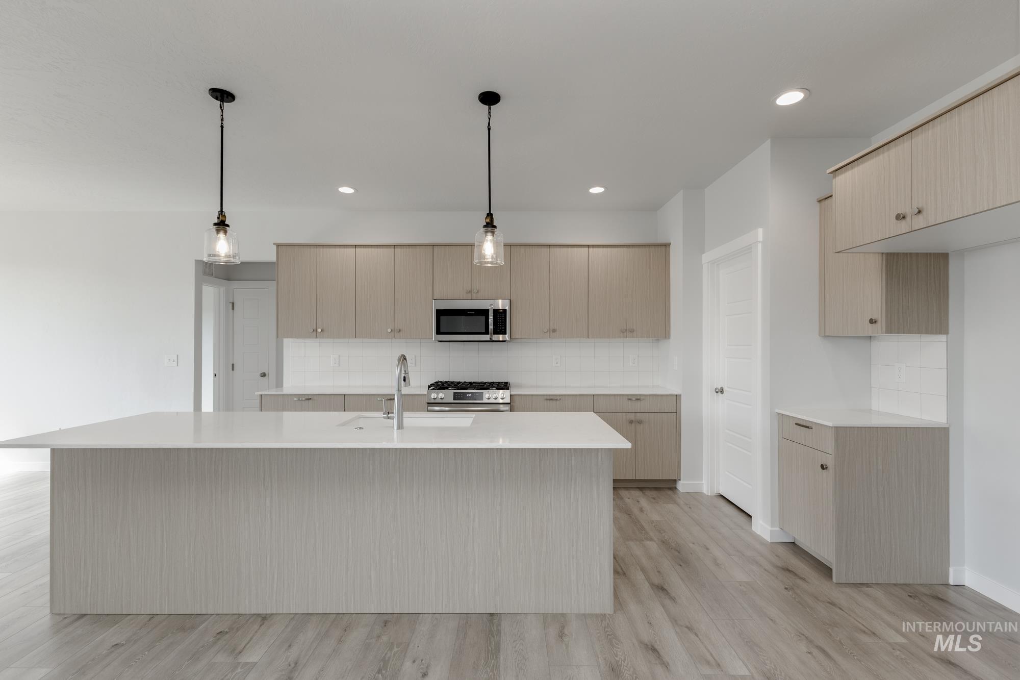 Kitchen featuring backsplash, an island with sink, light wood-style flooring, hanging light fixtures, and recessed lighting