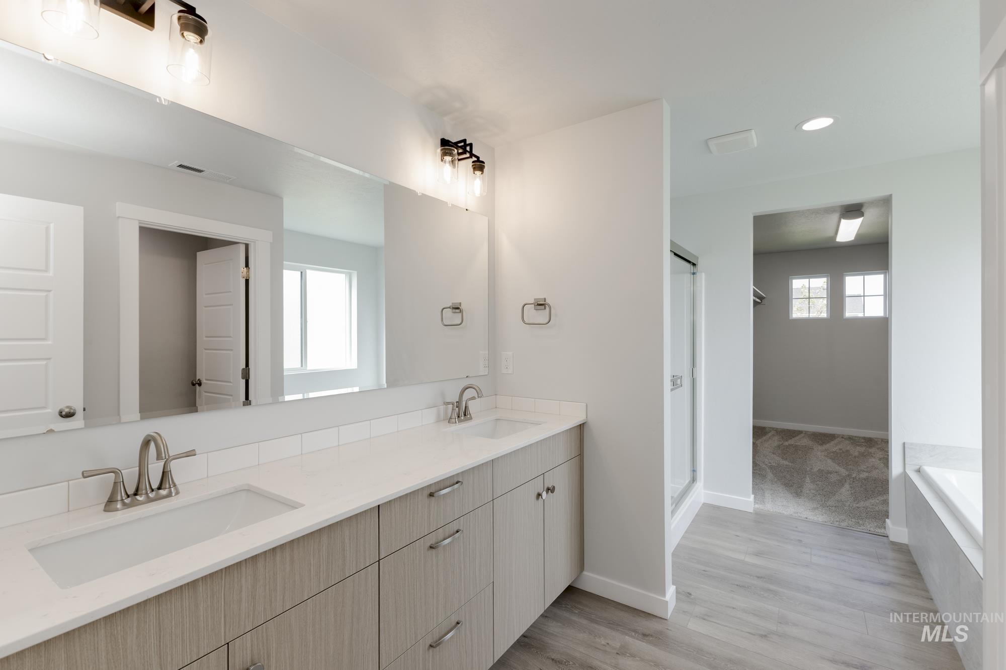 Full bath featuring plenty of natural light, double vanity, light wood-type flooring, recessed lighting, and a bath