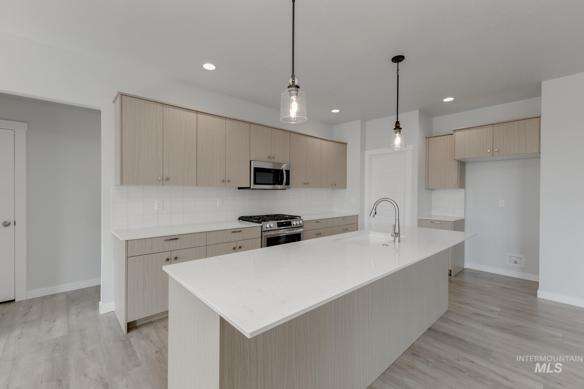 Kitchen with backsplash, light stone countertops, light brown cabinets, stainless steel appliances, and a kitchen island with sink