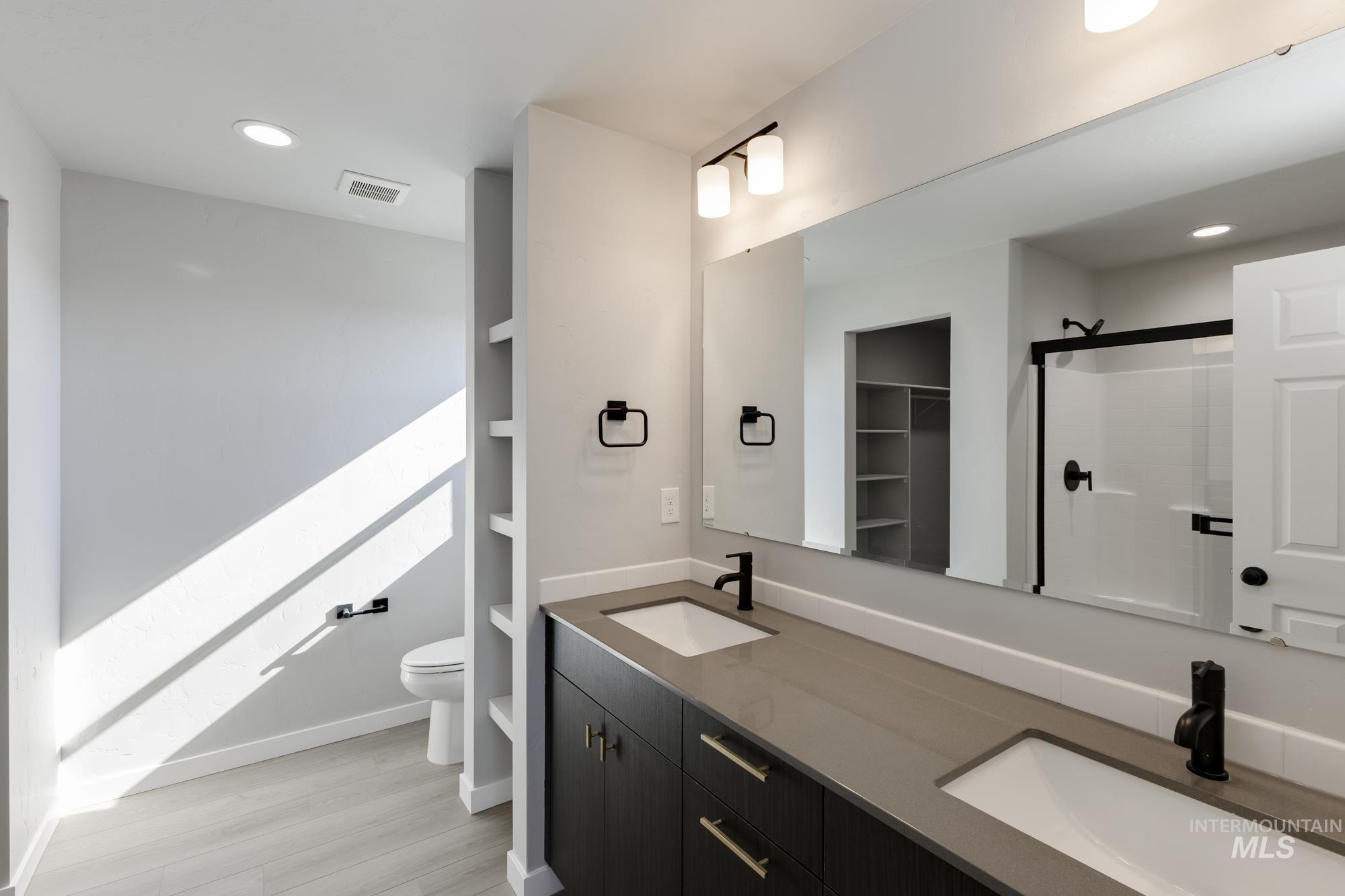 Full bath featuring recessed lighting, double vanity, a shower stall, a walk in closet, and light wood finished floors