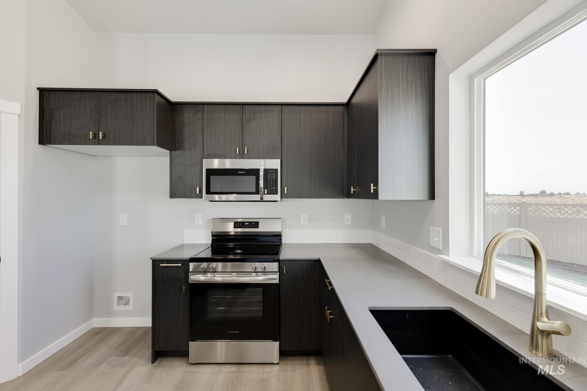 Kitchen with stainless steel appliances, light wood-type flooring, dark cabinetry, and light stone countertops