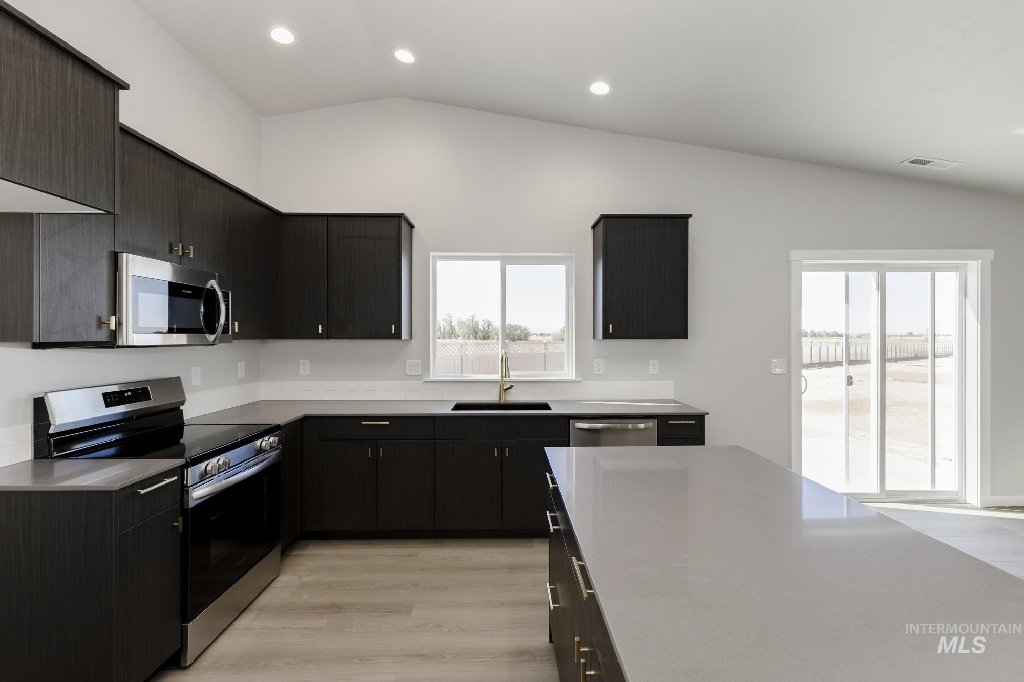 Kitchen with stainless steel appliances, vaulted ceiling, light wood-type flooring, recessed lighting, and dark cabinets