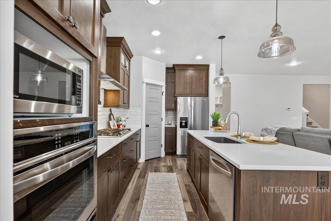 Kitchen with appliances with stainless steel finishes, decorative light fixtures, a kitchen island with sink, decorative backsplash, and dark wood-style floors