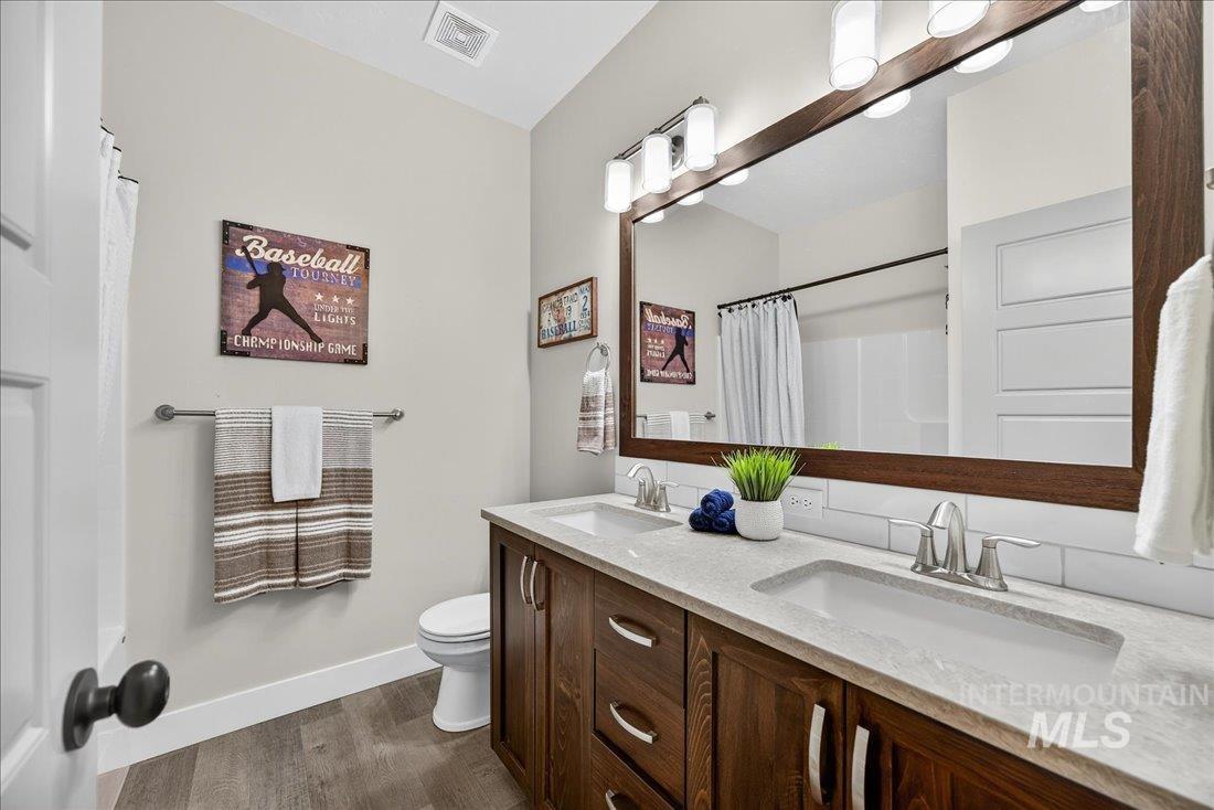 Full bathroom featuring double vanity, dark wood-style flooring, and curtained shower