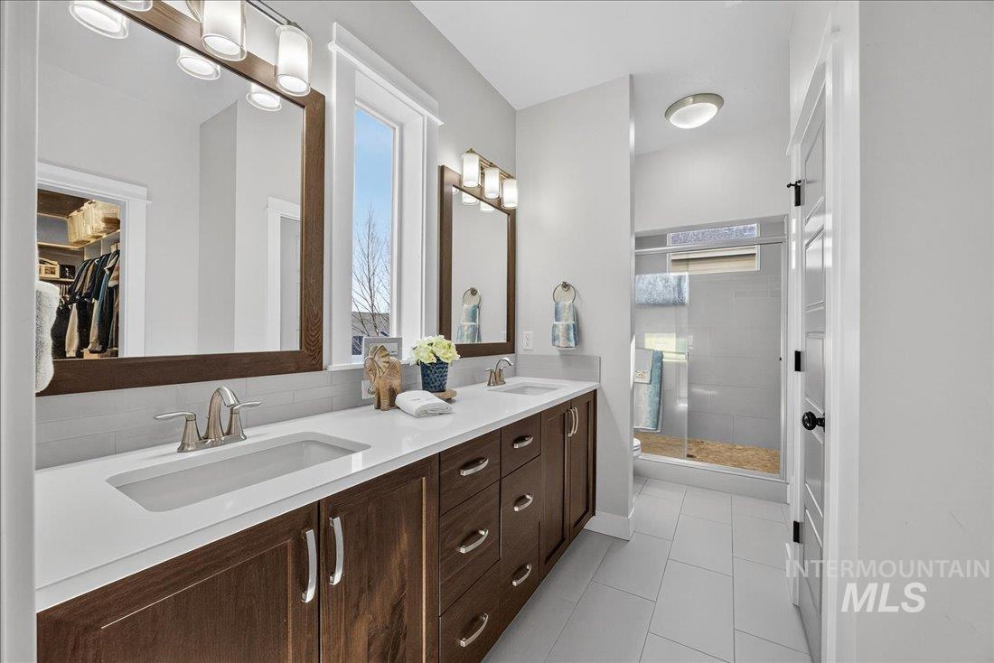 Full bathroom featuring double vanity, a spacious closet, a stall shower, light tile patterned floors, and decorative backsplash
