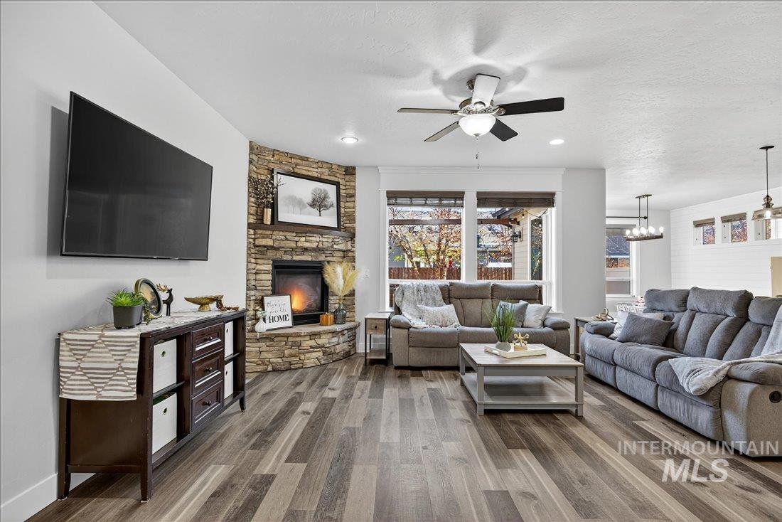 Living area featuring a stone fireplace, a ceiling fan, wood finished floors, a textured ceiling, and recessed lighting