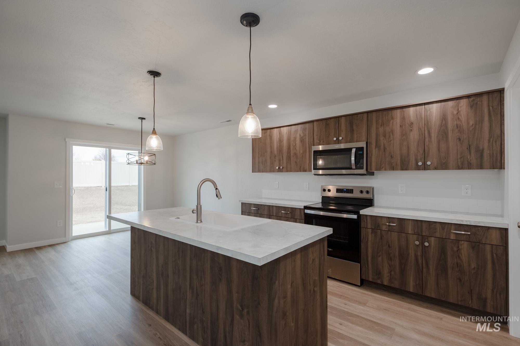 Kitchen featuring stainless steel appliances, light countertops, hanging light fixtures, dark brown cabinets, and a kitchen island with sink