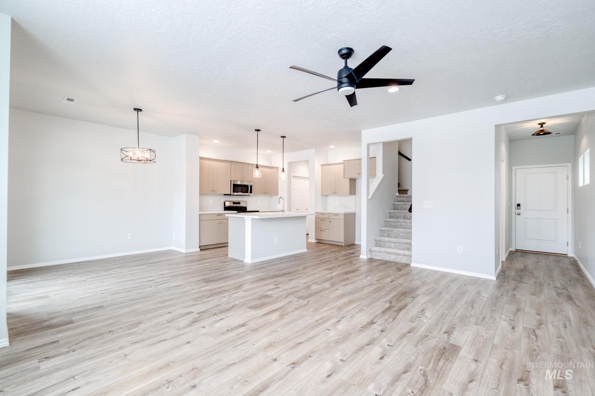 Unfurnished living room with ceiling fan, light wood finished floors, a chandelier, and stairway
