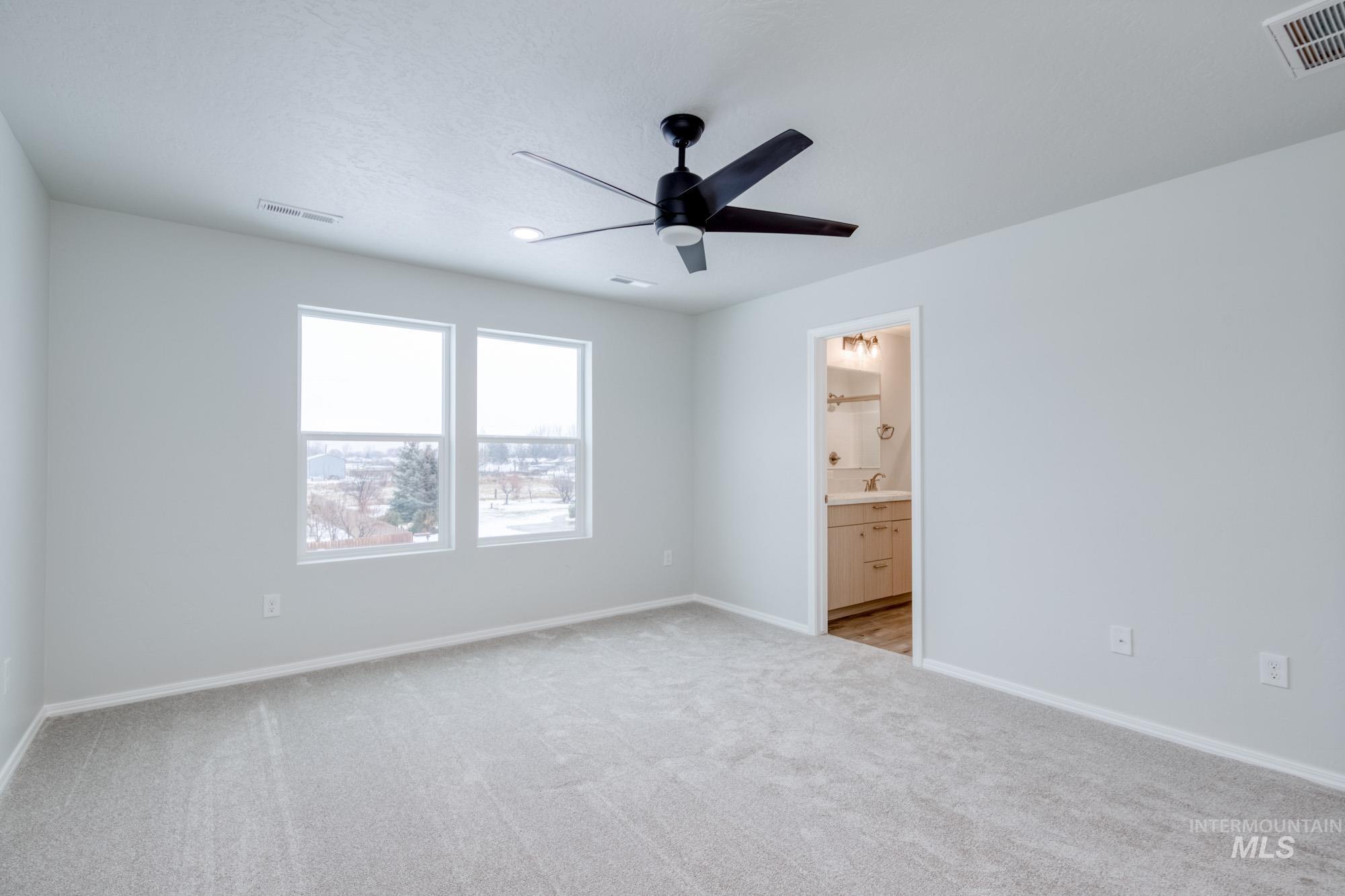 Unfurnished bedroom featuring light carpet, ceiling fan, and ensuite bath