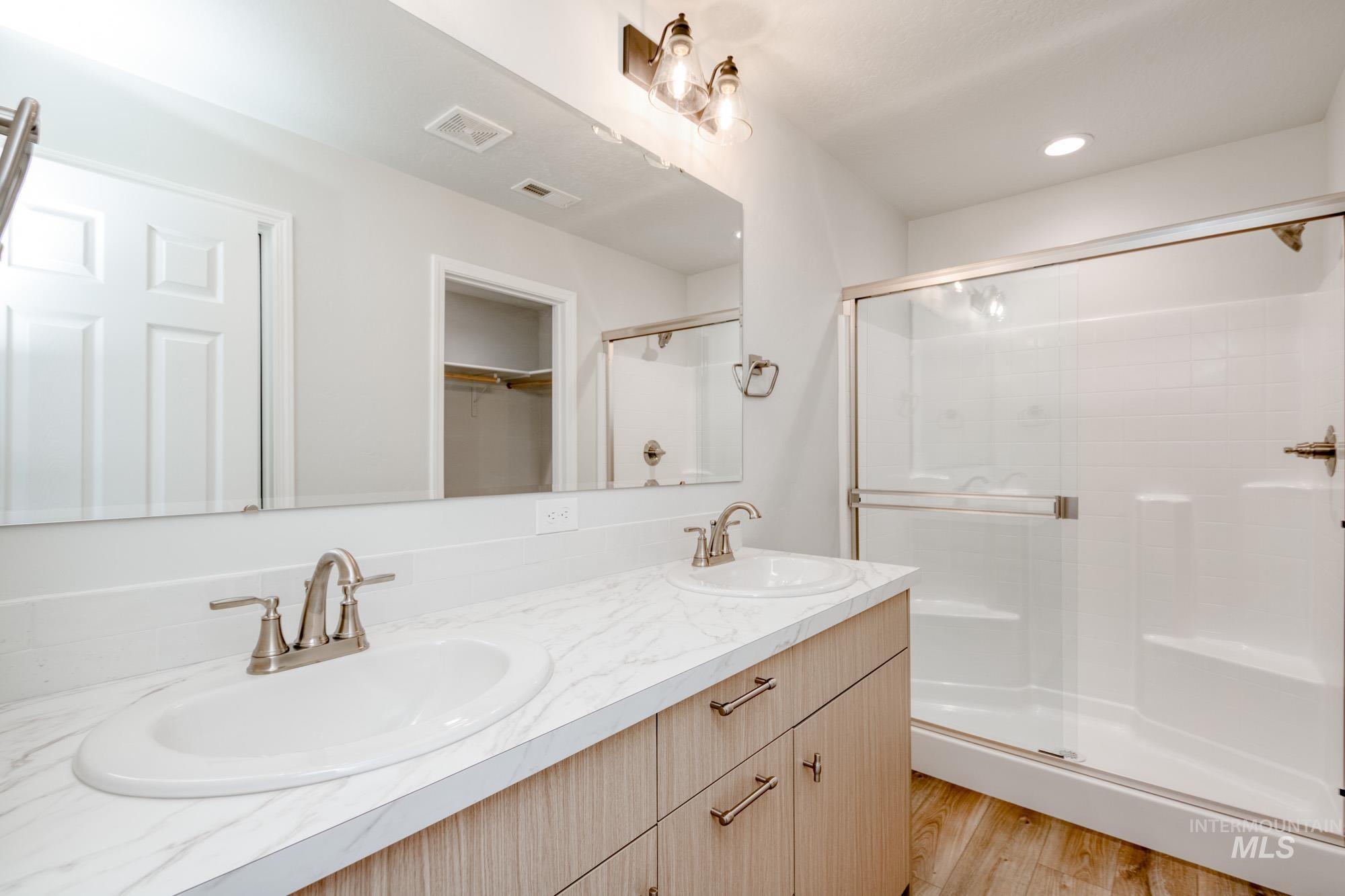 Full bath with a walk in closet, double vanity, light wood-type flooring, a shower stall, and recessed lighting