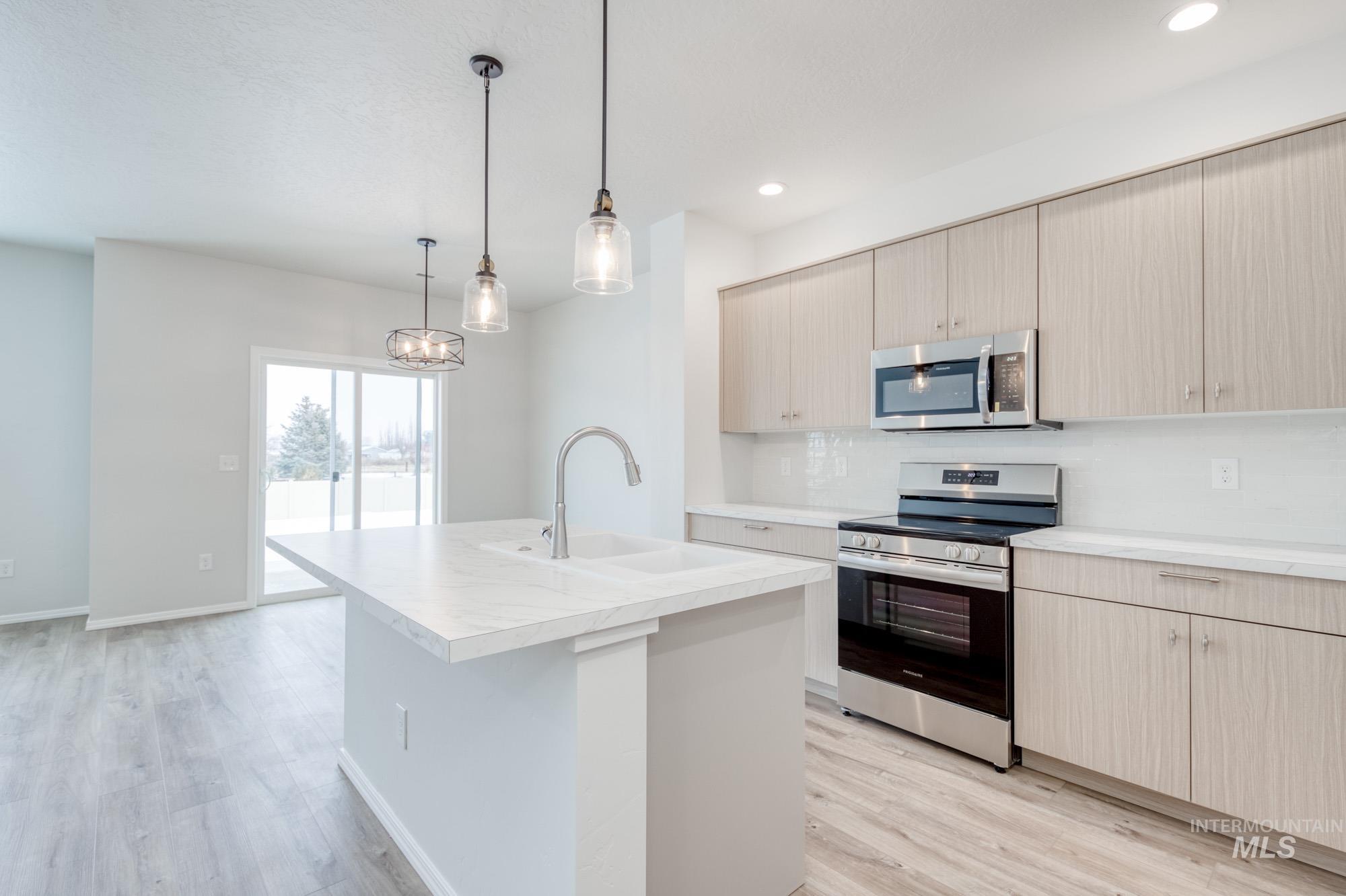 Kitchen featuring appliances with stainless steel finishes, light countertops, hanging light fixtures, light wood finished floors, and light brown cabinets