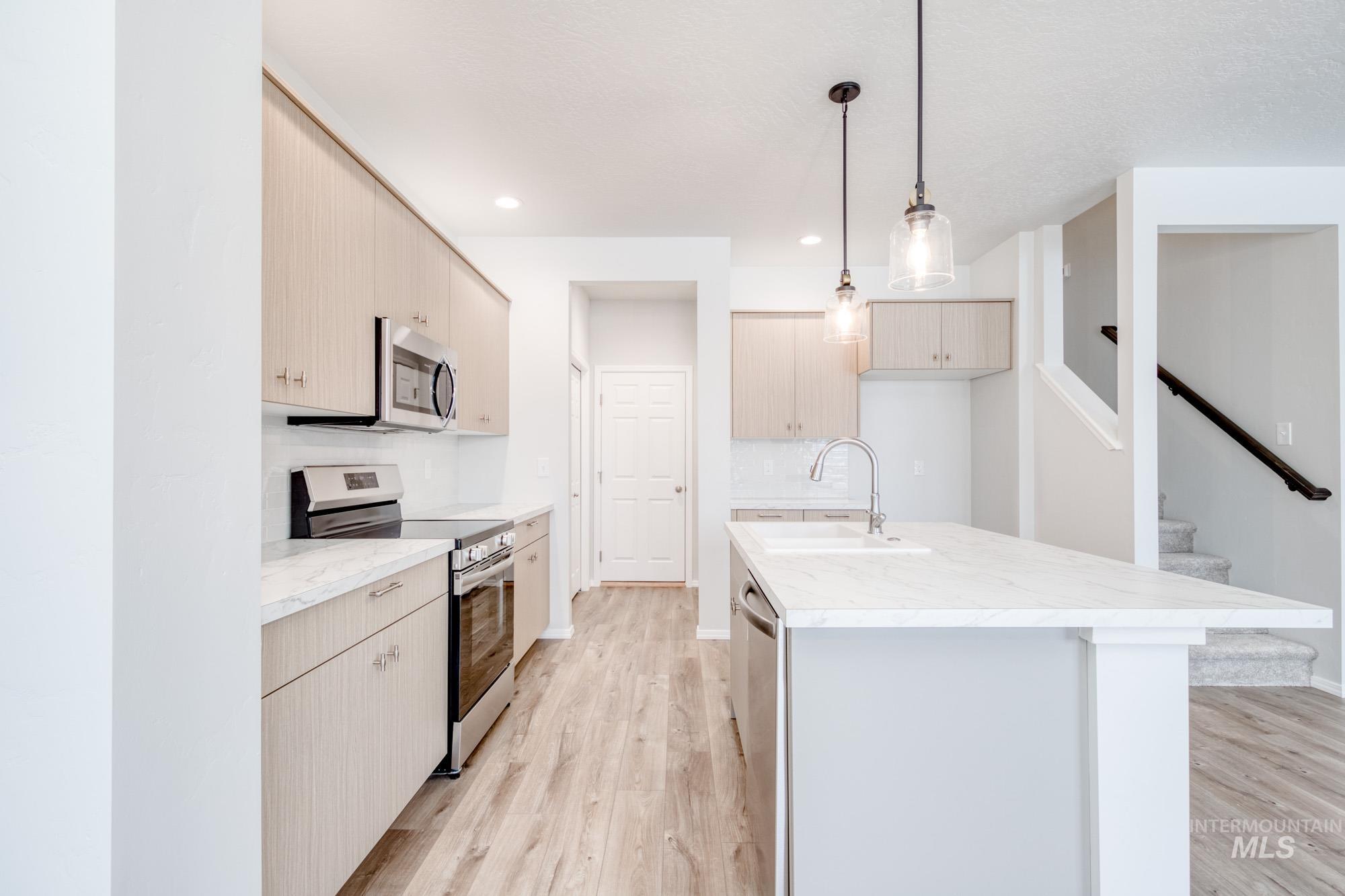 Kitchen featuring appliances with stainless steel finishes, decorative light fixtures, light wood-type flooring, a center island with sink, and recessed lighting