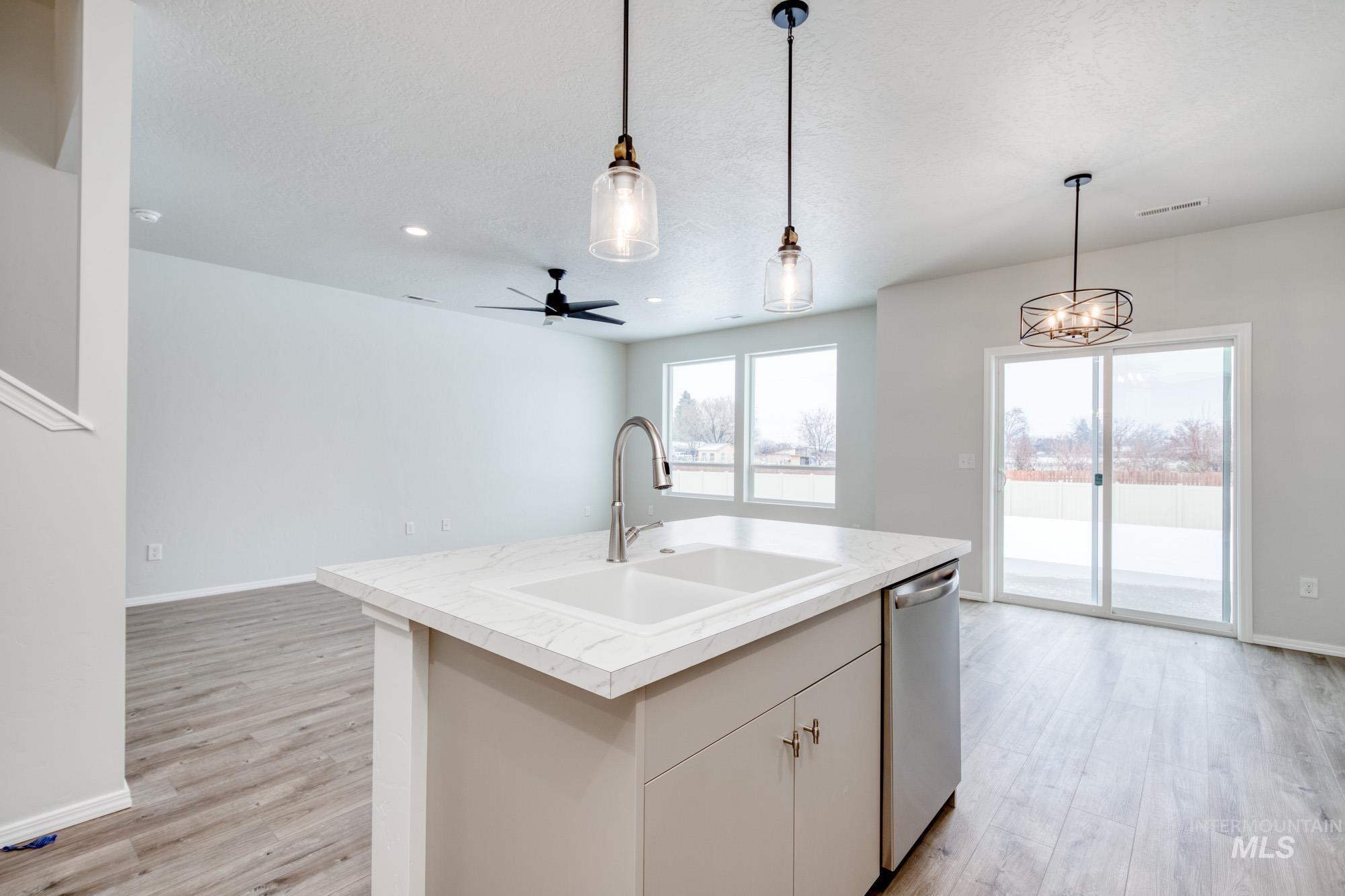 Kitchen featuring light countertops, hanging light fixtures, open floor plan, light wood-style flooring, and stainless steel dishwasher