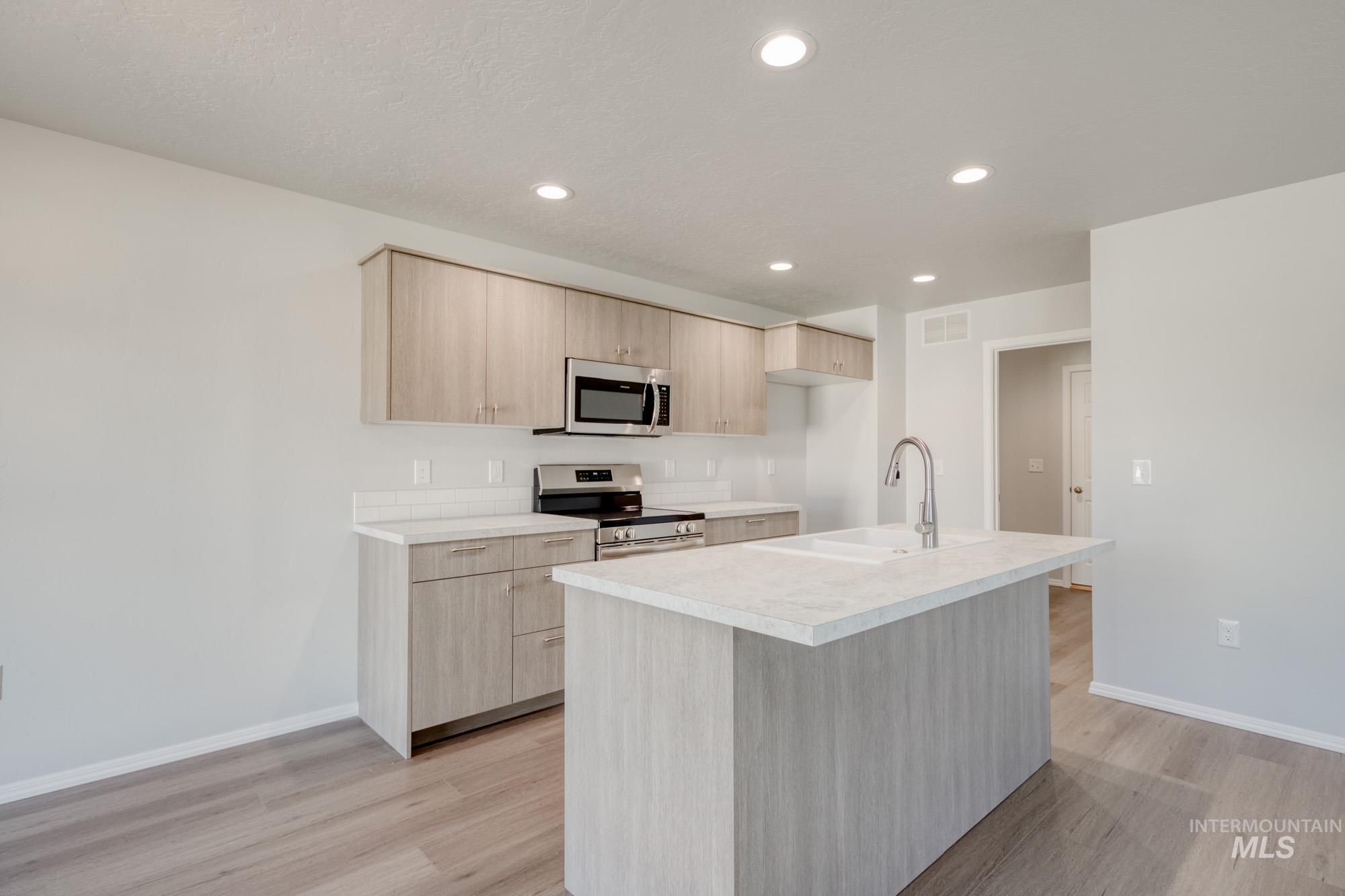 Kitchen with light brown cabinetry, light countertops, stainless steel appliances, a center island with sink, and recessed lighting