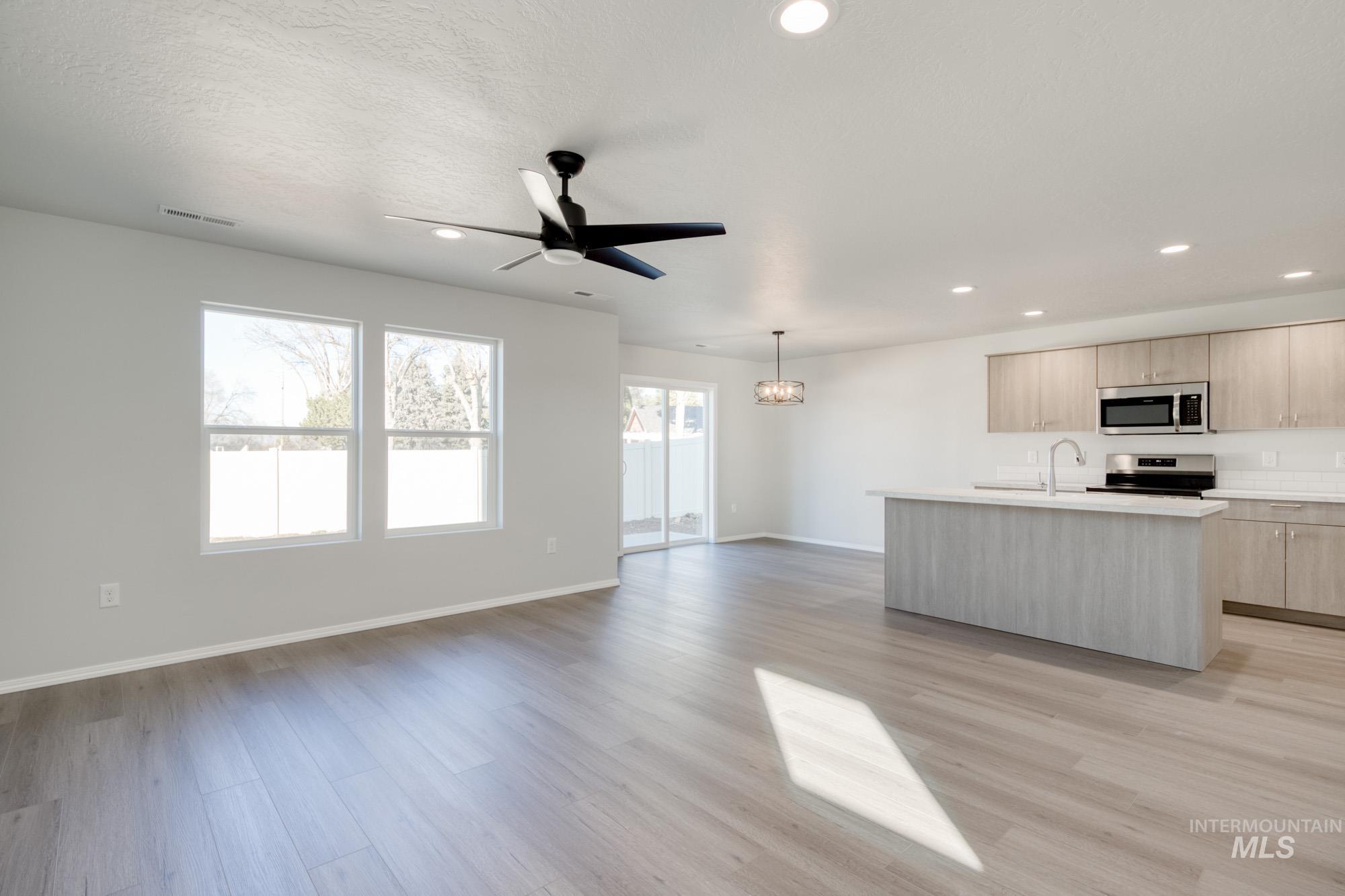 Kitchen featuring a kitchen island with sink, open floor plan, stainless steel appliances, light wood finished floors, and decorative light fixtures