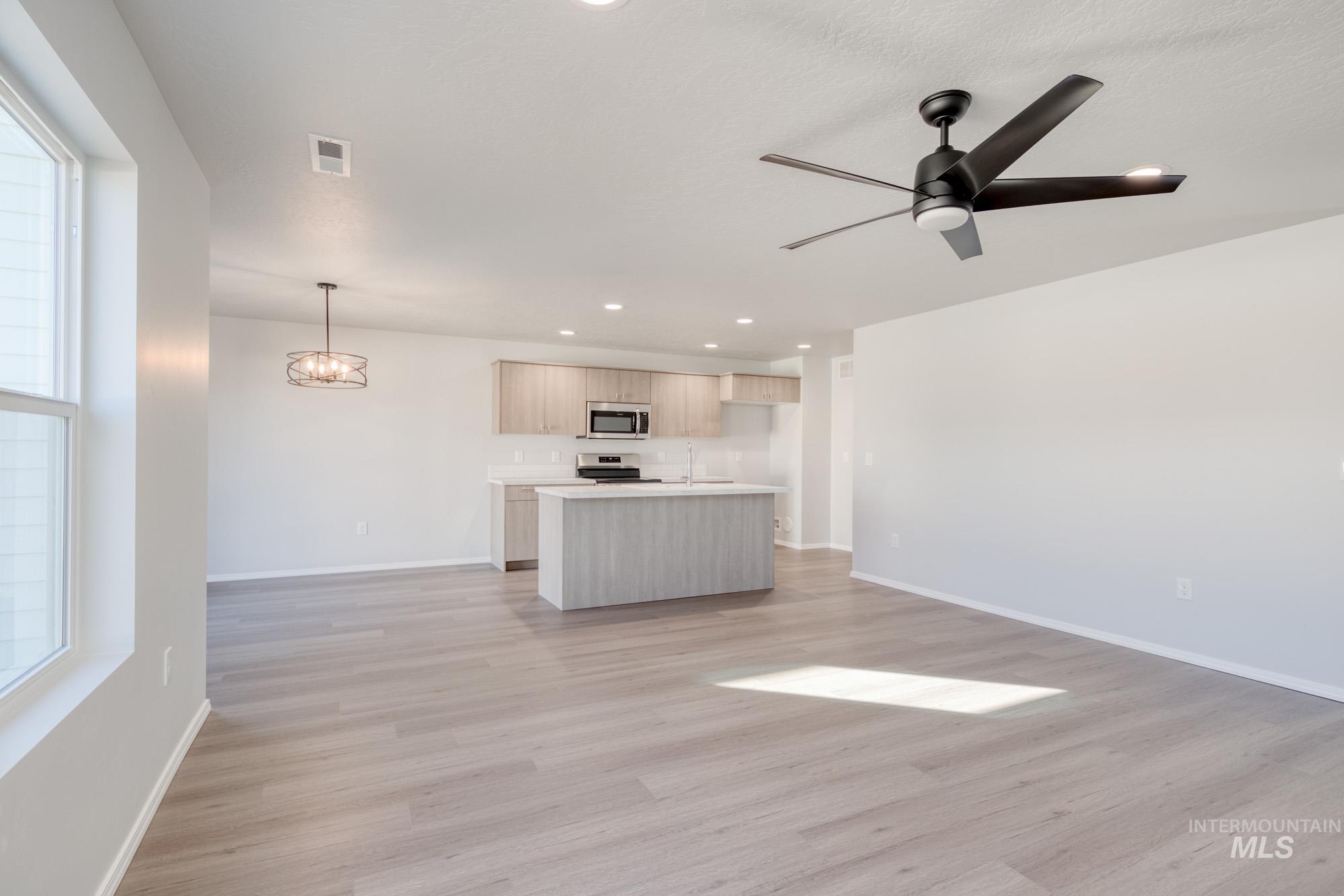 Unfurnished living room featuring recessed lighting, light wood finished floors, a chandelier, and a ceiling fan