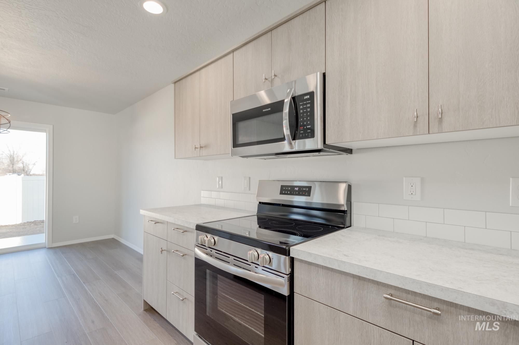 Kitchen with stainless steel appliances, light brown cabinets, light wood finished floors, modern cabinets, and a textured ceiling