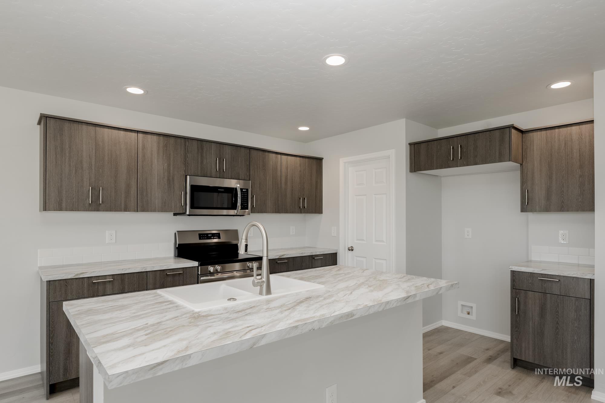 Kitchen with light countertops, dark brown cabinets, light wood-style floors, appliances with stainless steel finishes, and modern cabinets