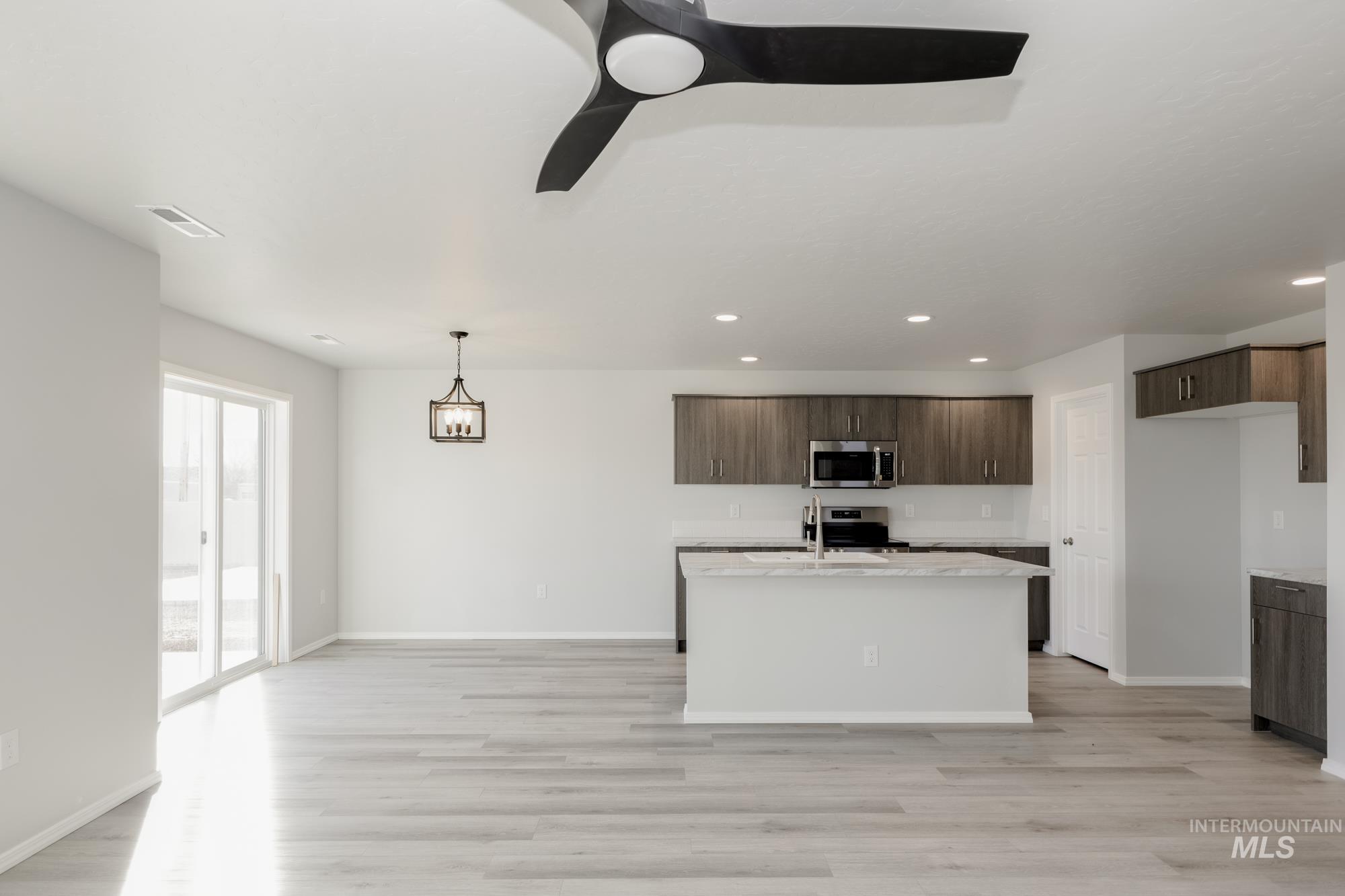 Kitchen with dark brown cabinets, light wood finished floors, recessed lighting, decorative light fixtures, and appliances with stainless steel finishes