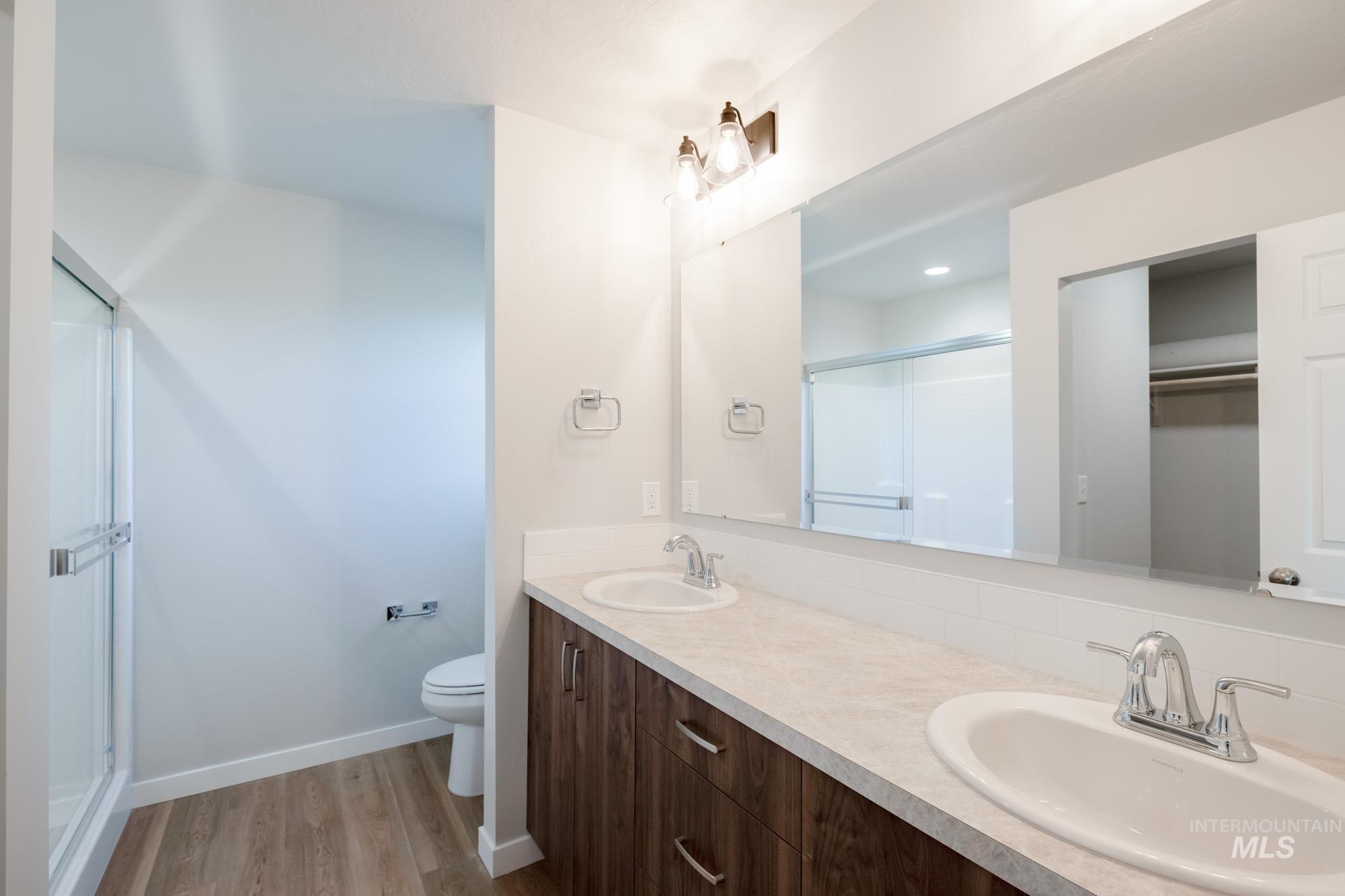 Full bath featuring double vanity, a shower stall, light wood-type flooring, and a spacious closet