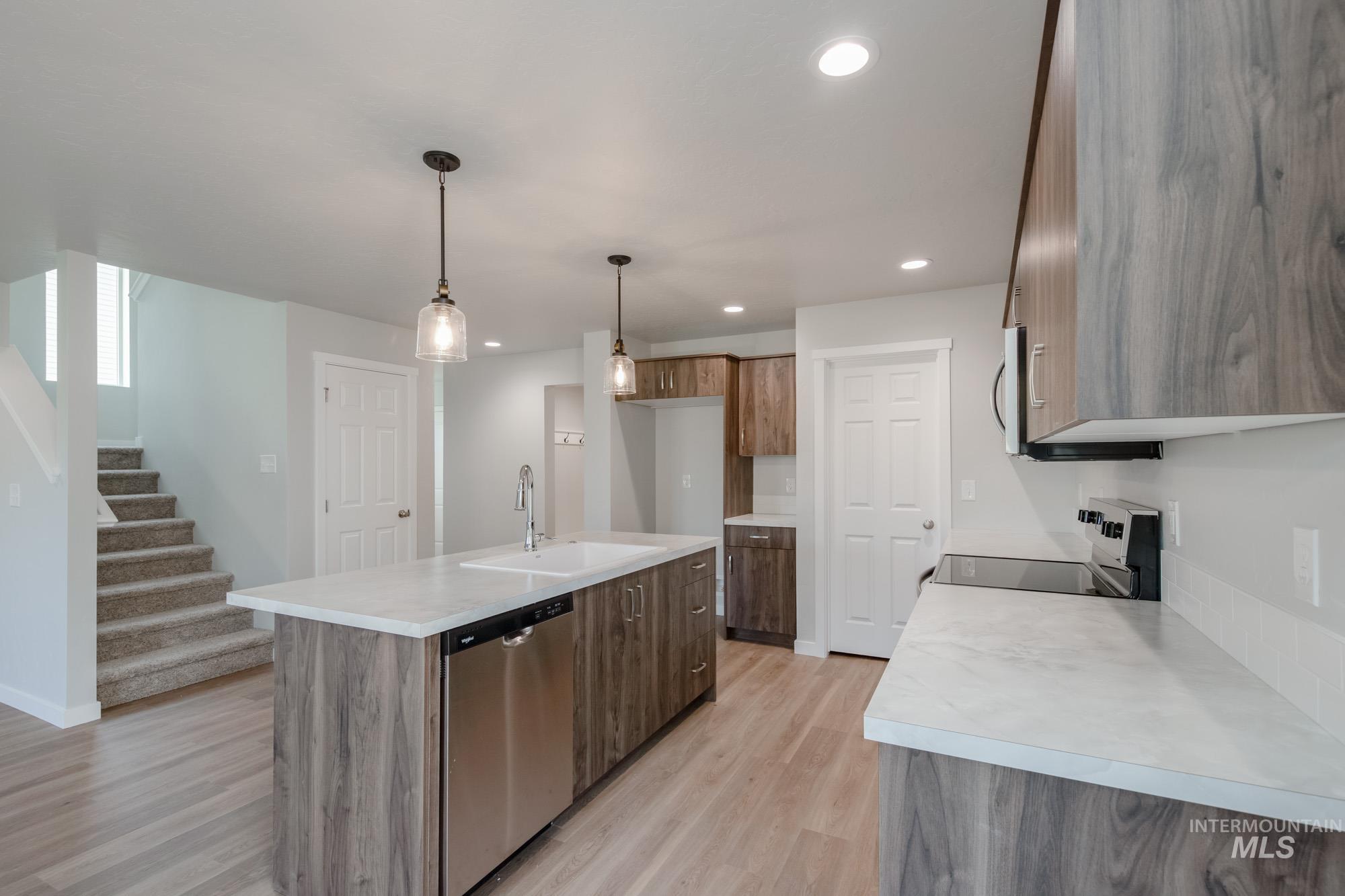 Kitchen featuring light countertops, stainless steel appliances, recessed lighting, hanging light fixtures, and an island with sink