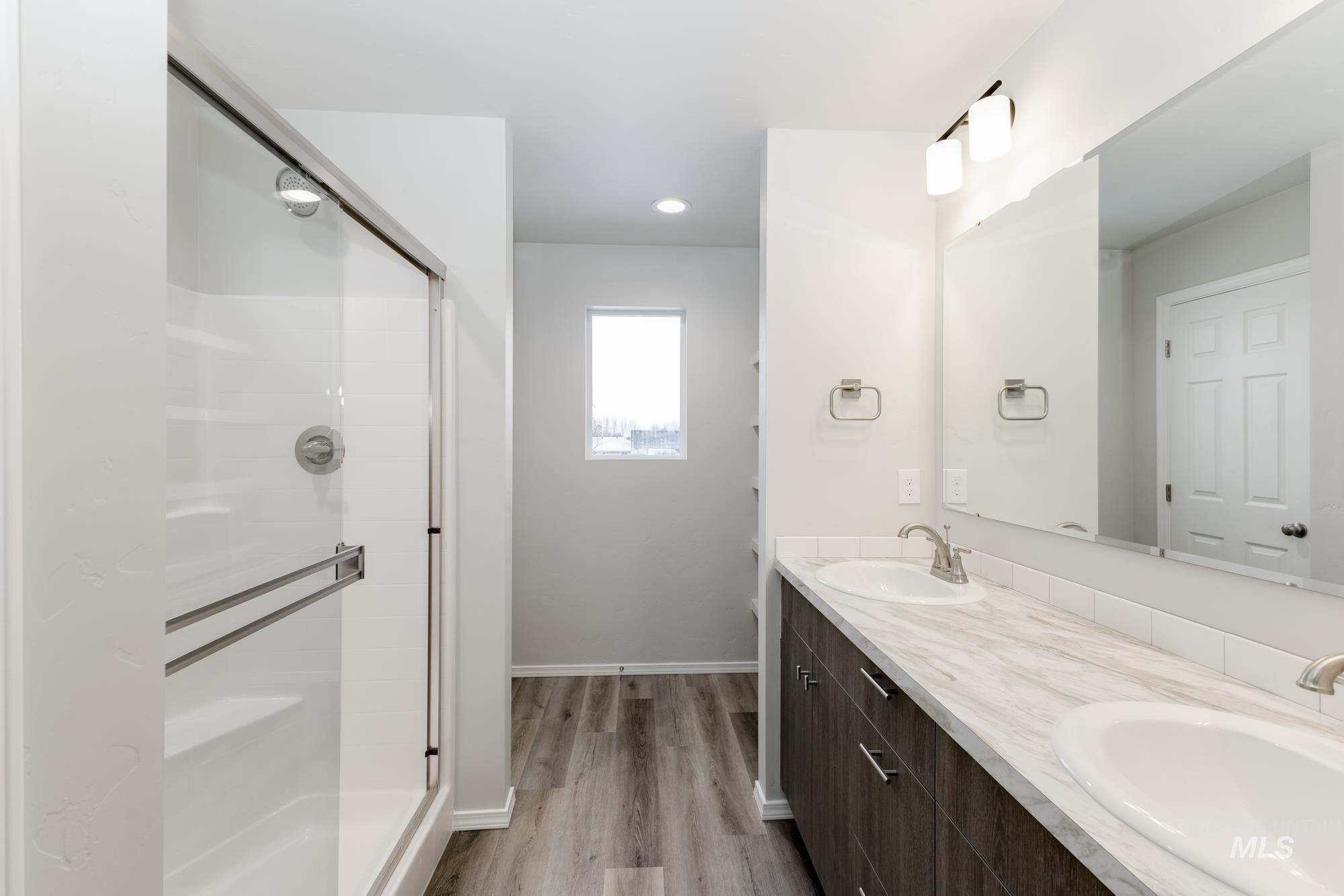 Bathroom featuring double vanity, light wood finished floors, a shower stall, and recessed lighting