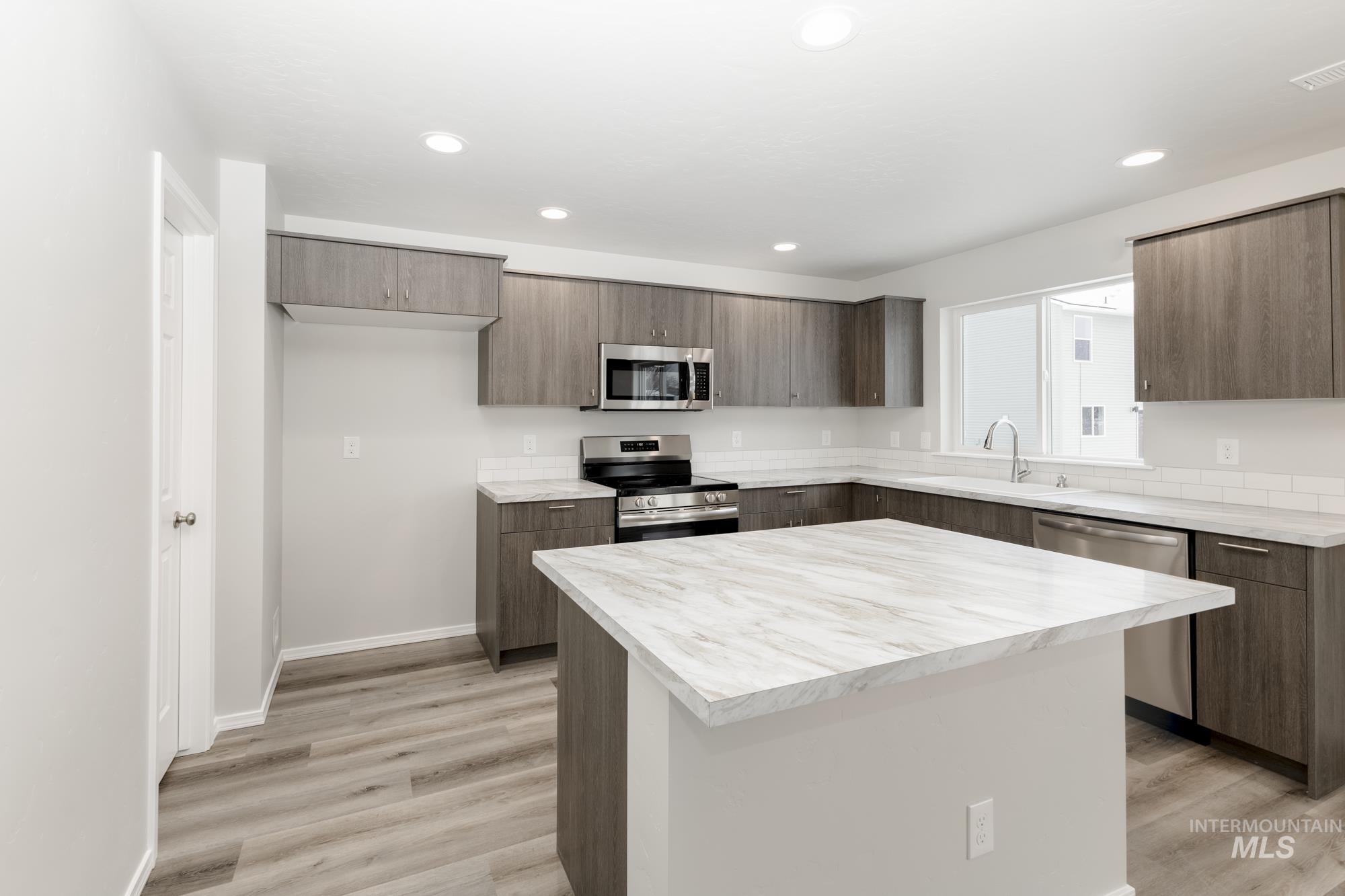 Kitchen featuring light countertops, stainless steel appliances, modern cabinets, a center island, and light wood finished floors