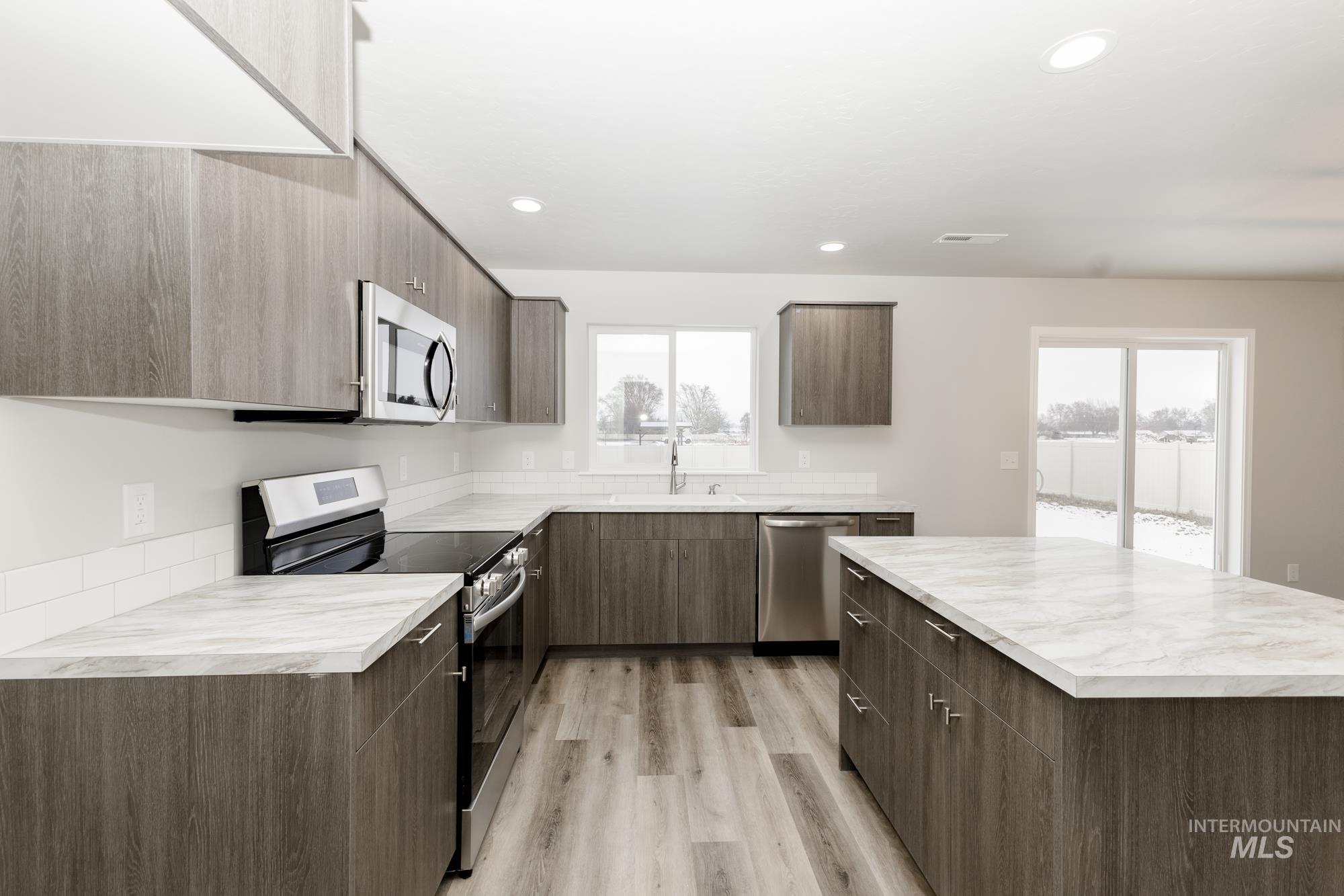 Kitchen with stainless steel appliances, a kitchen island, light countertops, modern cabinets, and recessed lighting