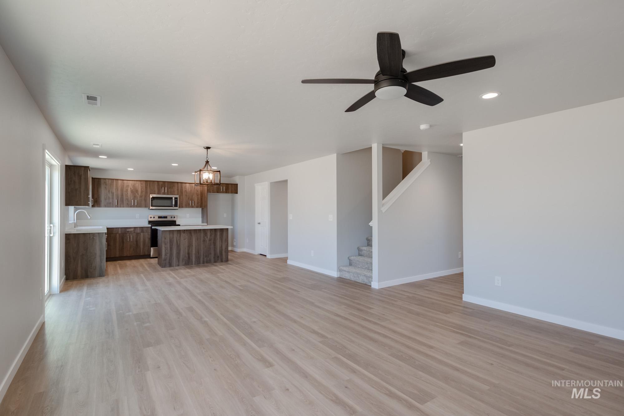 Unfurnished living room with recessed lighting, light wood-style floors, a ceiling fan, a chandelier, and stairway