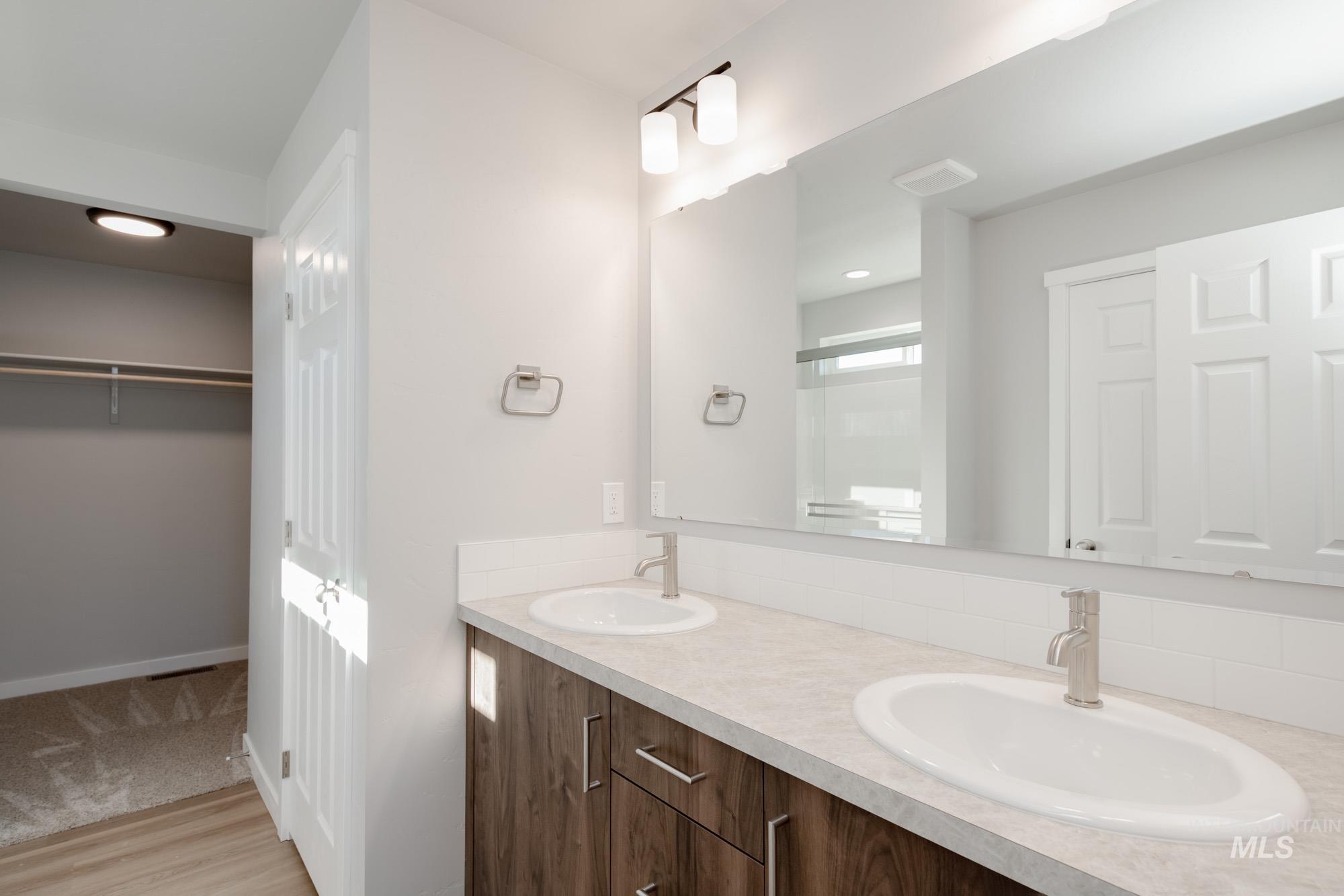 Bathroom with double vanity, a walk in closet, a stall shower, light wood-type flooring, and recessed lighting