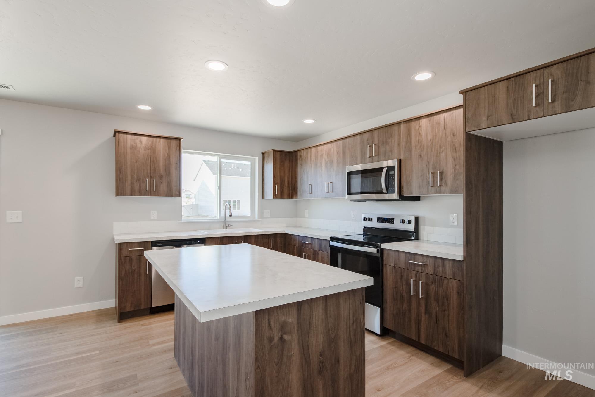 Kitchen with appliances with stainless steel finishes, light countertops, a kitchen island, light wood-style flooring, and recessed lighting