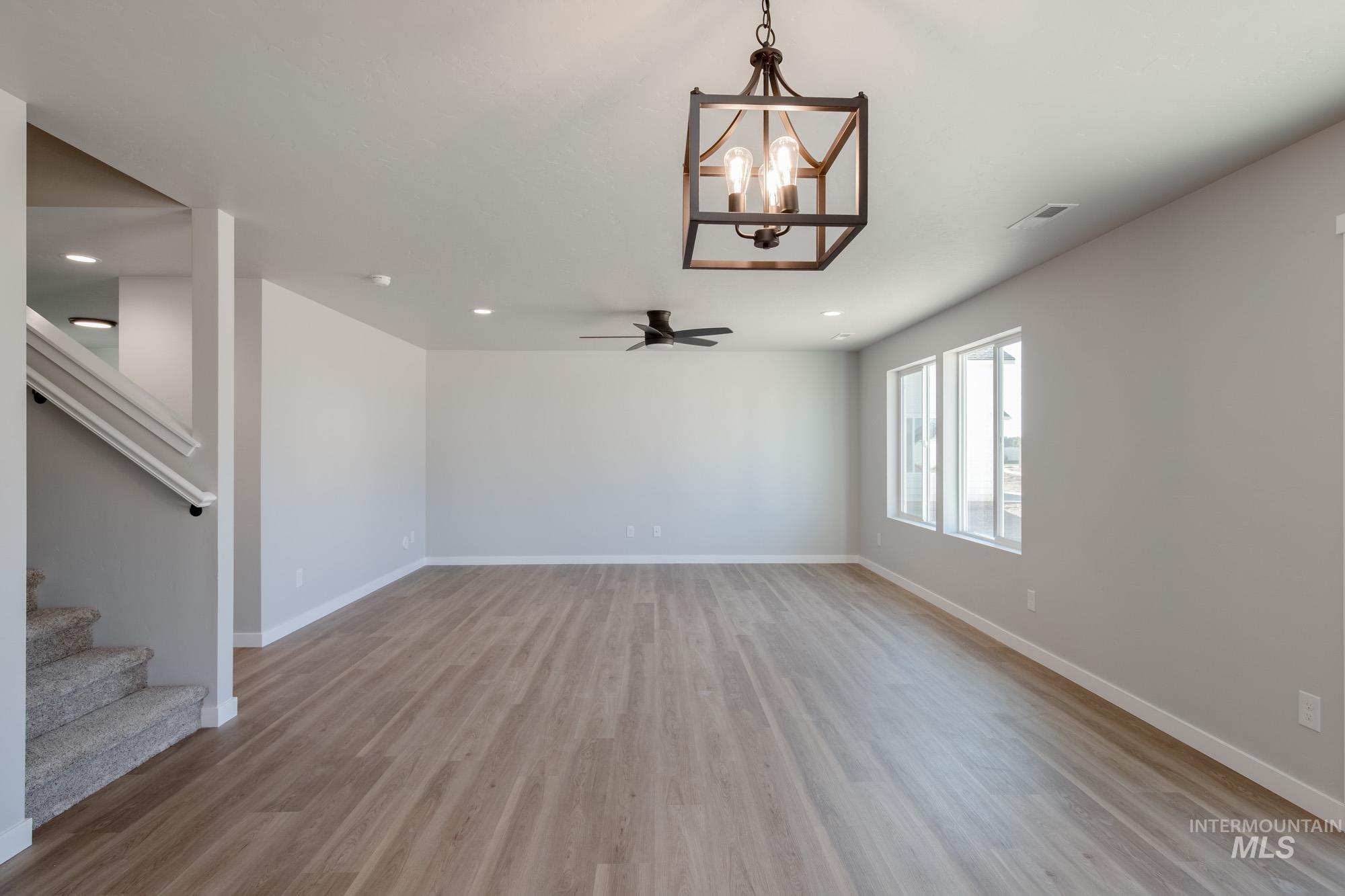Unfurnished living room with a chandelier, light wood-type flooring, stairway, recessed lighting, and ceiling fan