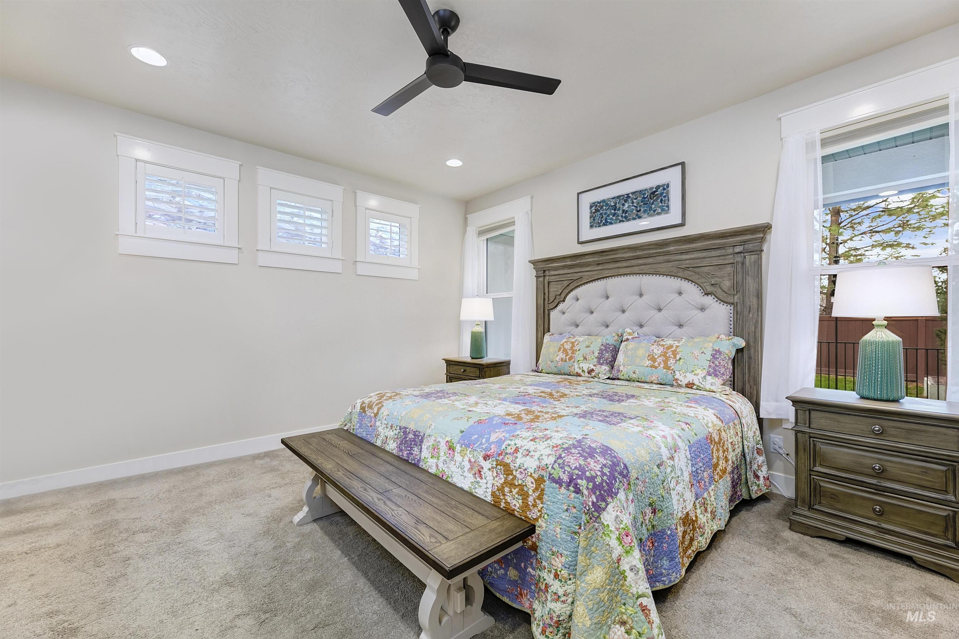 Bedroom featuring light colored carpet, multiple windows, and a ceiling fan