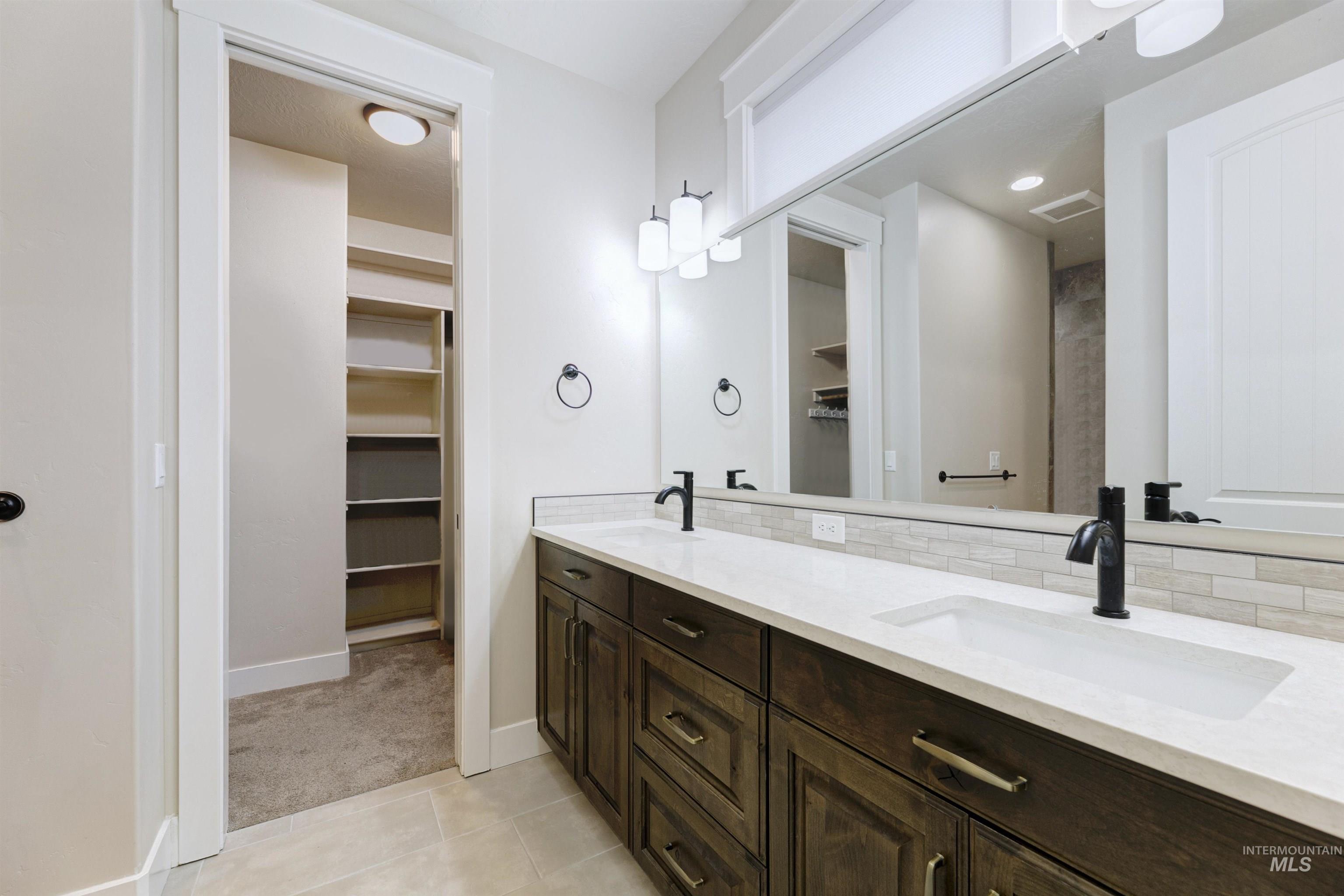 Full bathroom featuring a spacious closet, double vanity, light tile patterned flooring, and light colored carpet