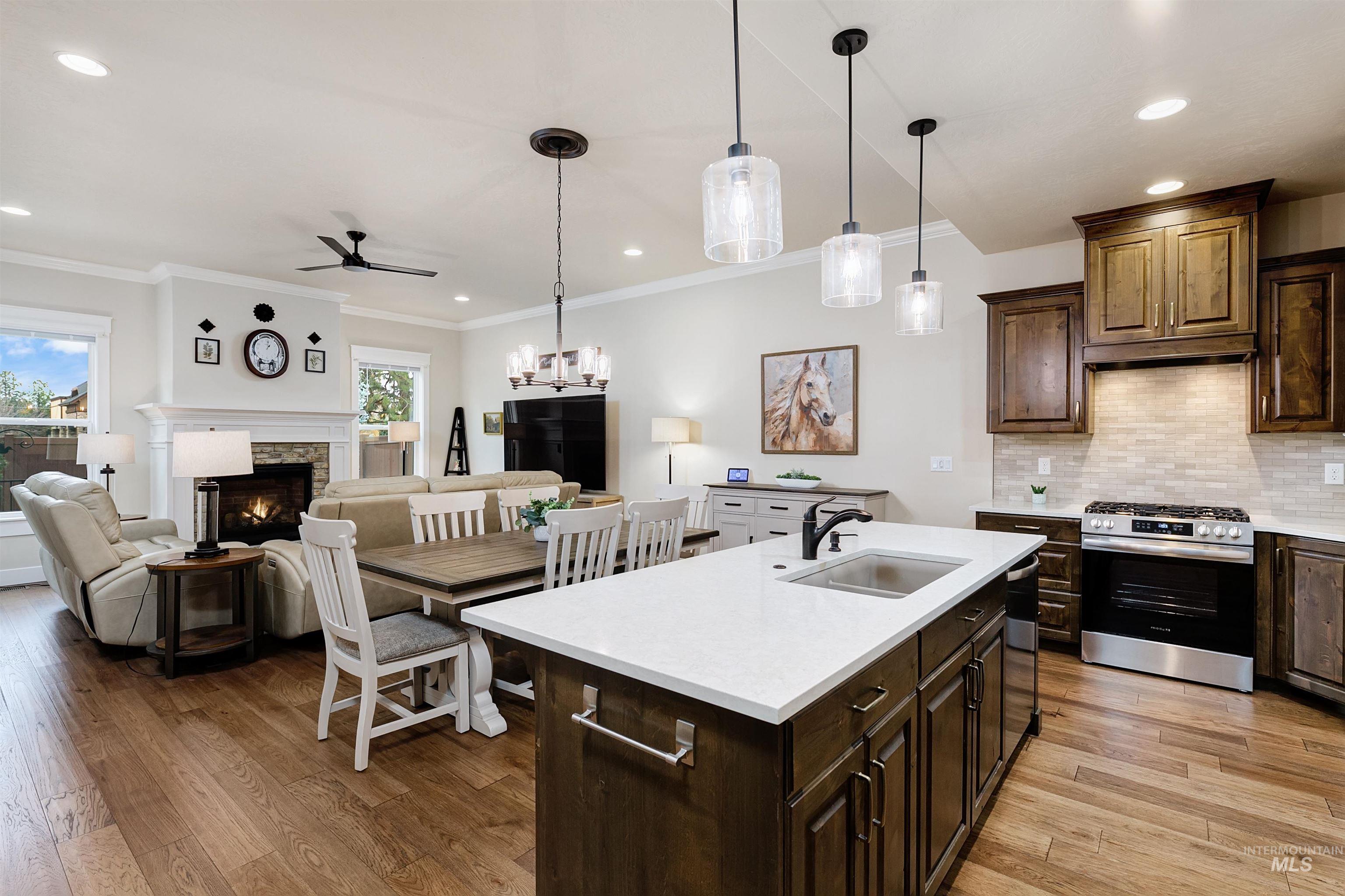 Kitchen with dark brown cabinets, stainless steel range with gas cooktop, decorative light fixtures, tasteful backsplash, and ornamental molding