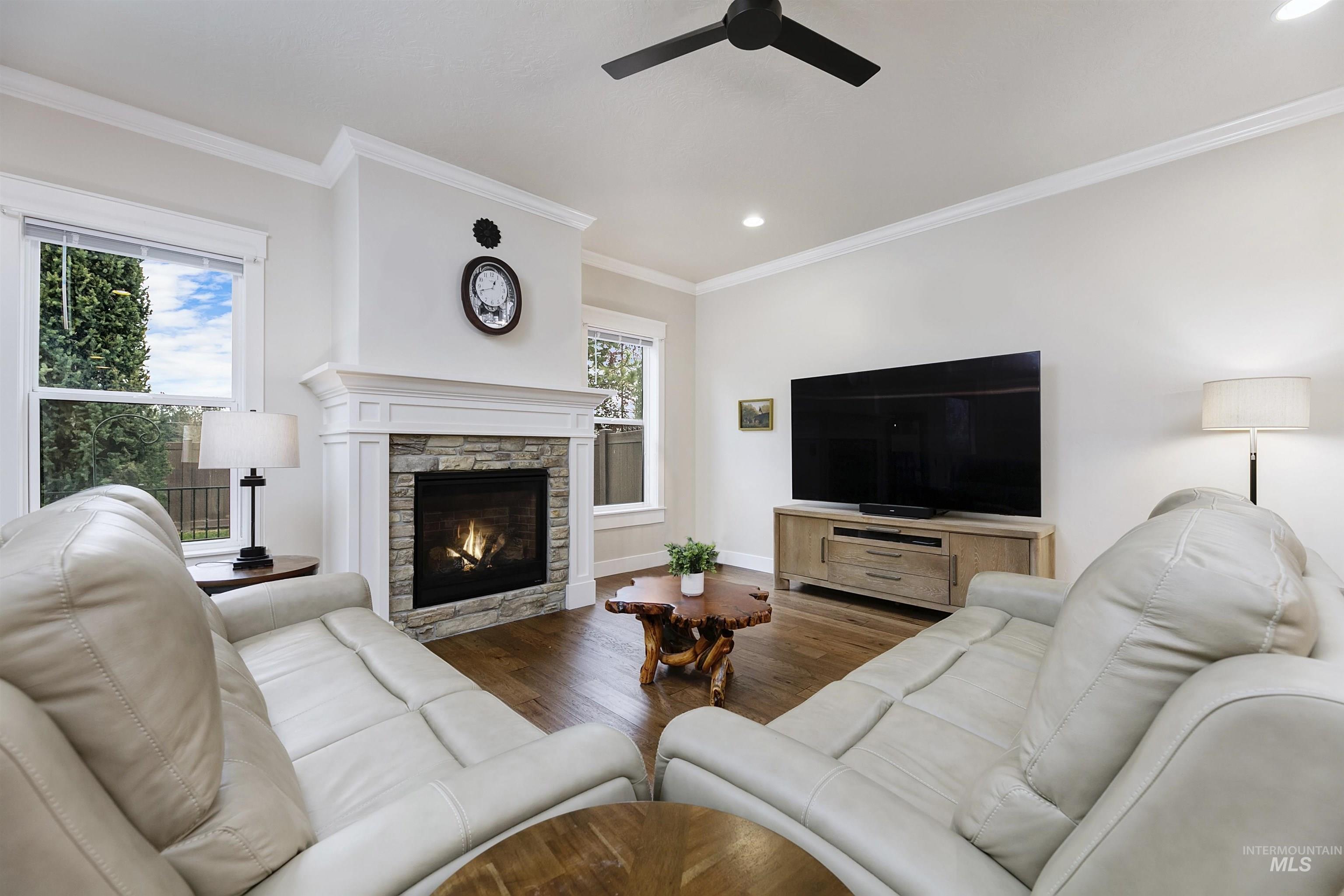 Living room featuring wood finished floors, a stone fireplace, ornamental molding, ceiling fan, and recessed lighting