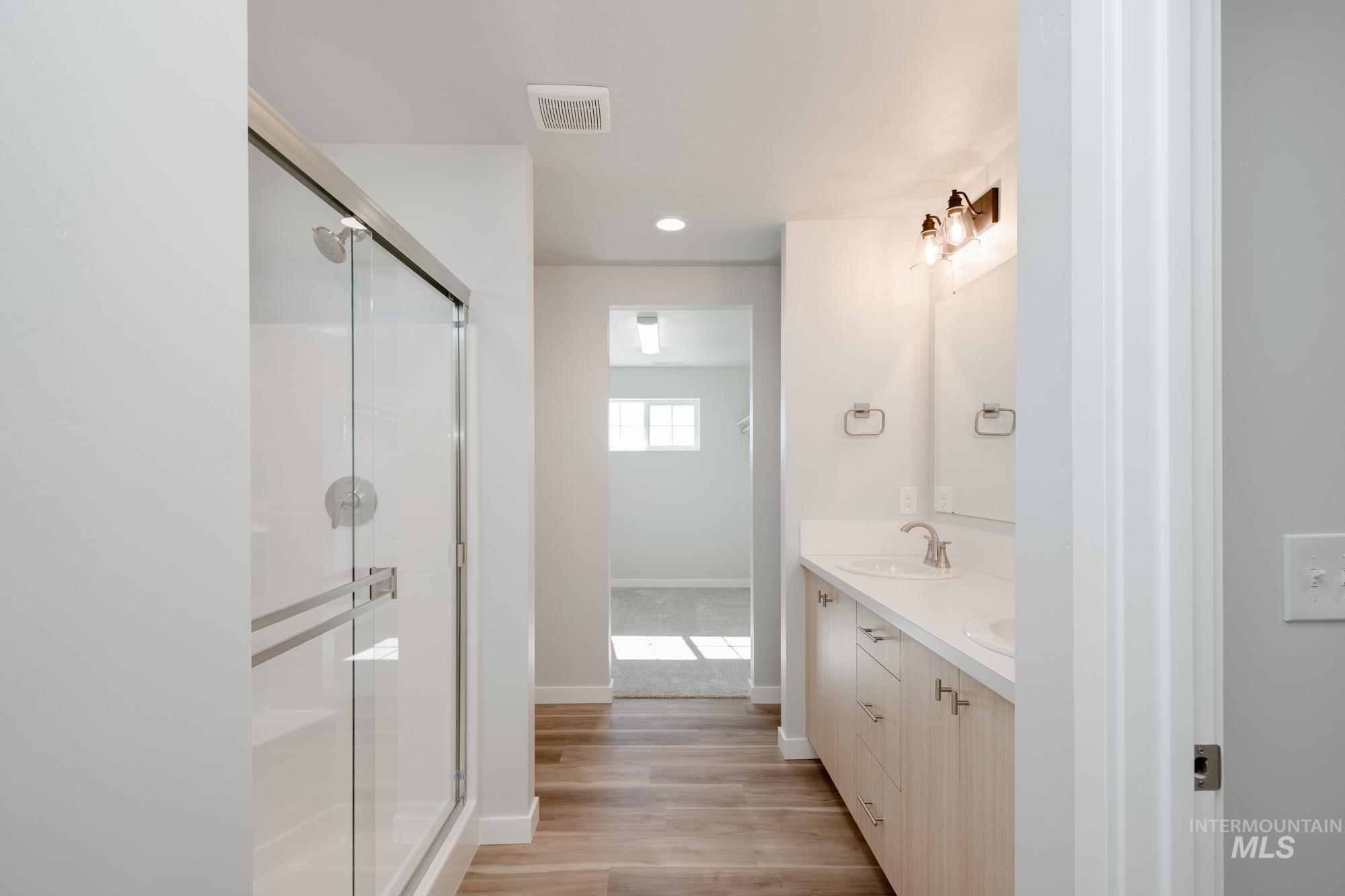 Full bathroom featuring double vanity, light wood finished floors, a stall shower, and recessed lighting
