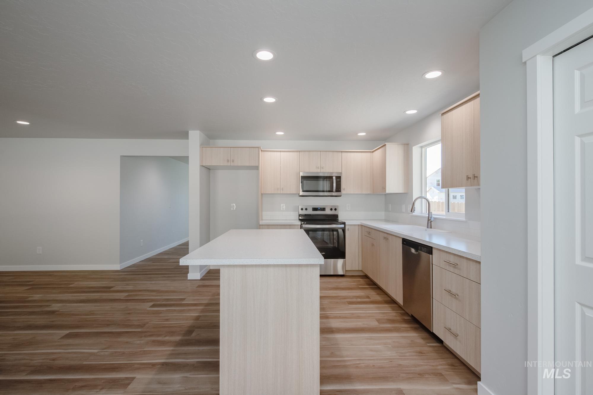 Kitchen with light brown cabinetry, stainless steel appliances, a kitchen island, light wood-type flooring, and recessed lighting