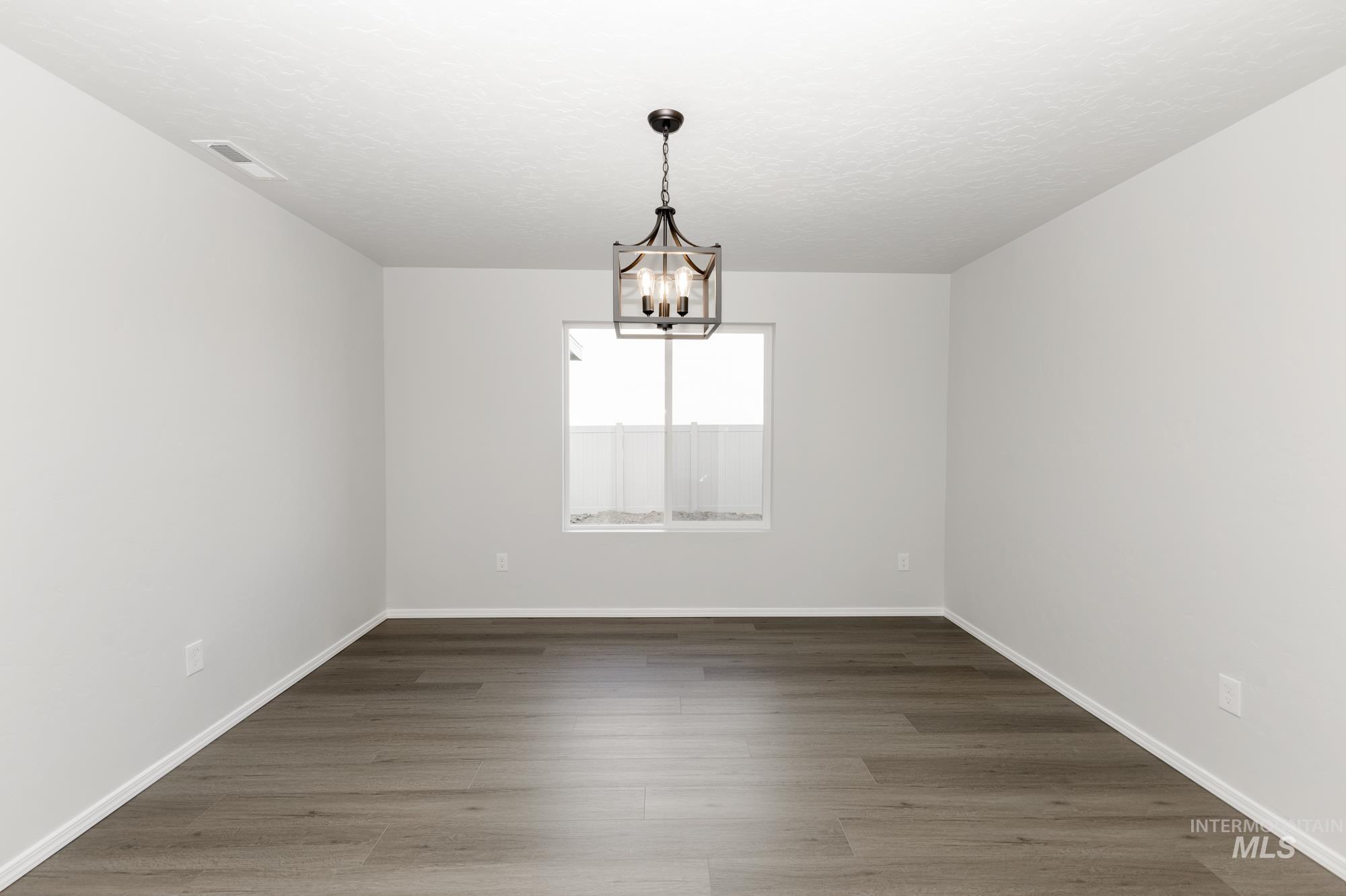Empty room featuring wood finished floors, a chandelier, and a textured ceiling