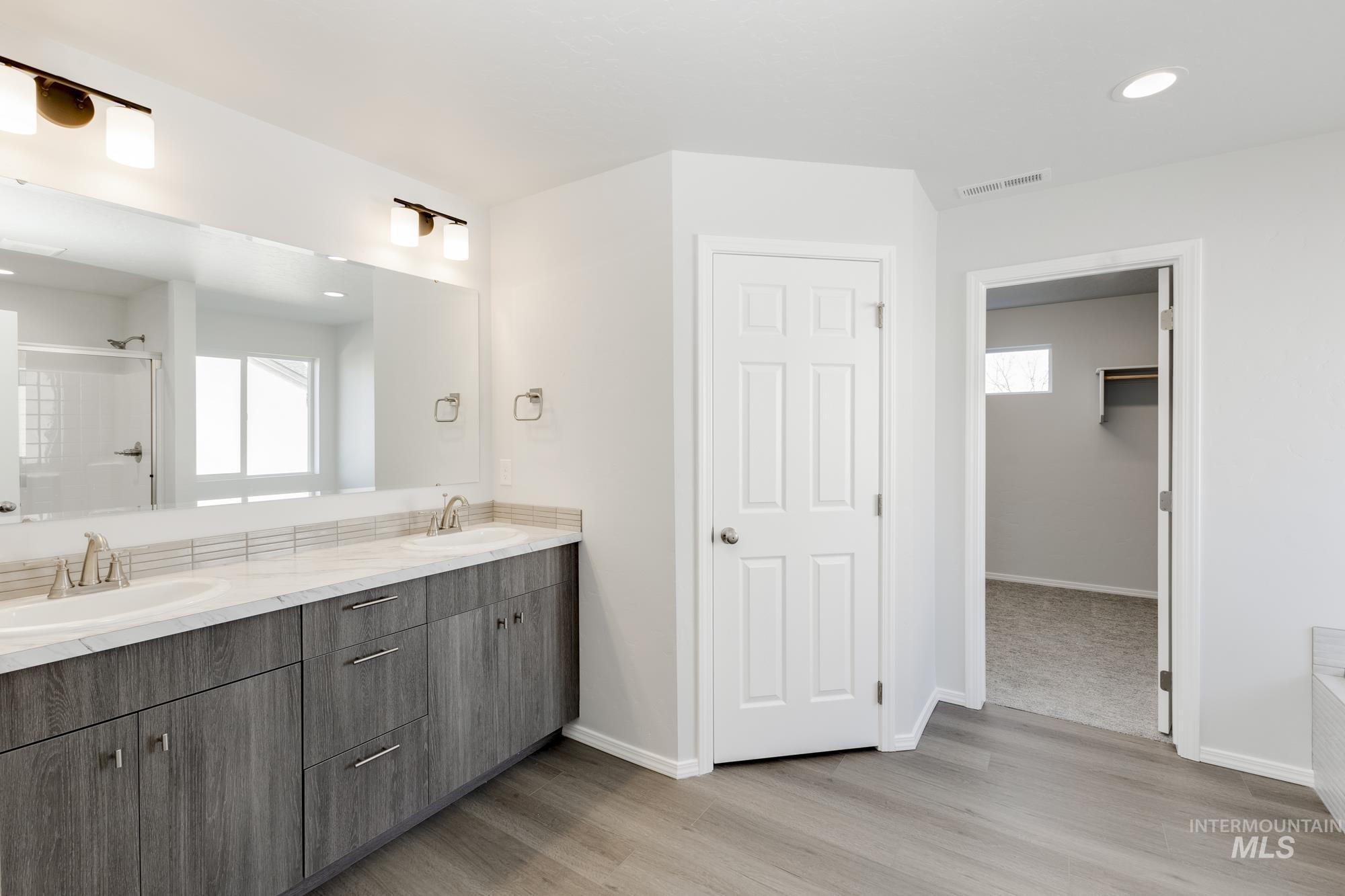 Full bathroom with a stall shower, double vanity, a spacious closet, recessed lighting, and light wood finished floors