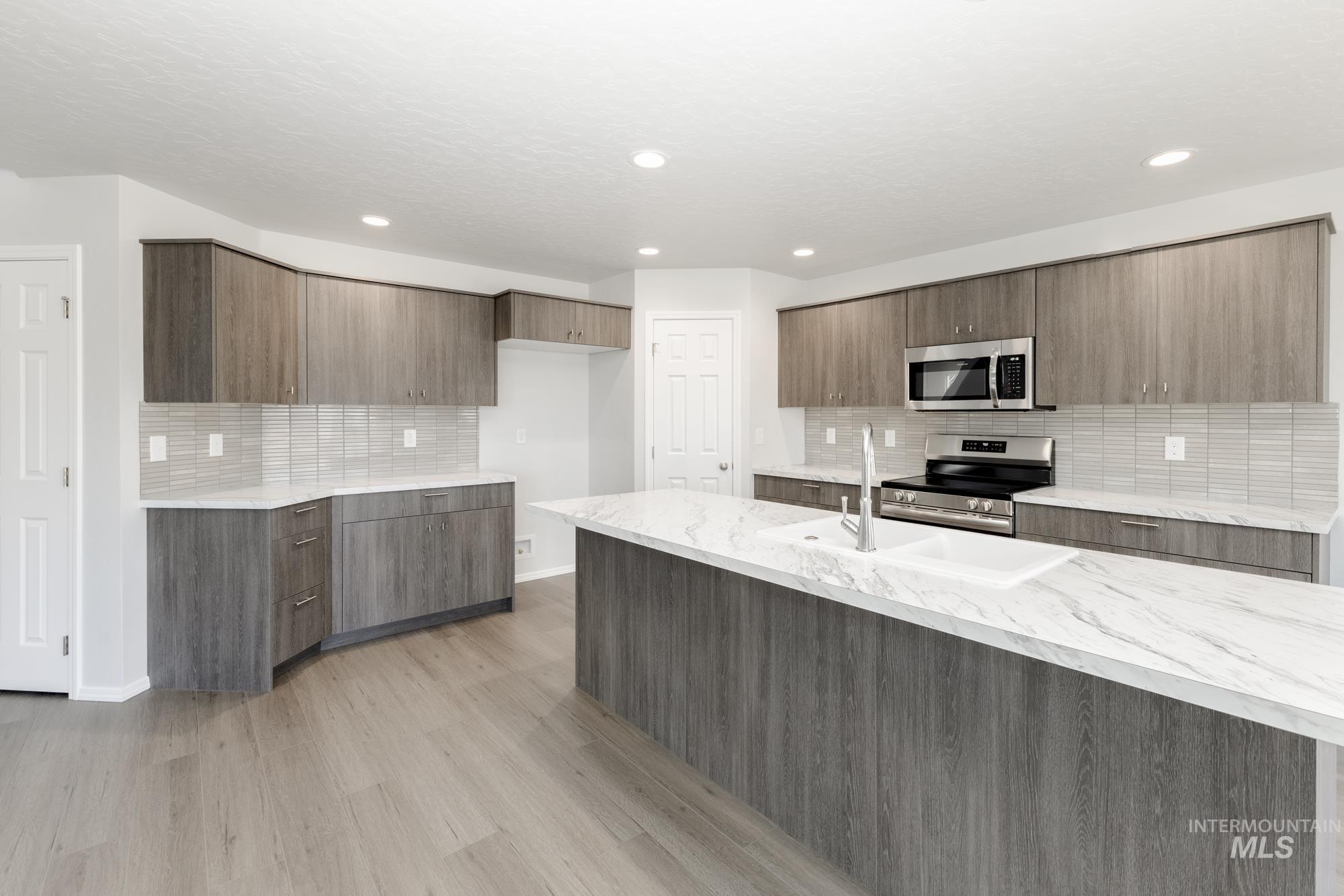 Kitchen with modern cabinets, light stone counters, stainless steel appliances, backsplash, and recessed lighting