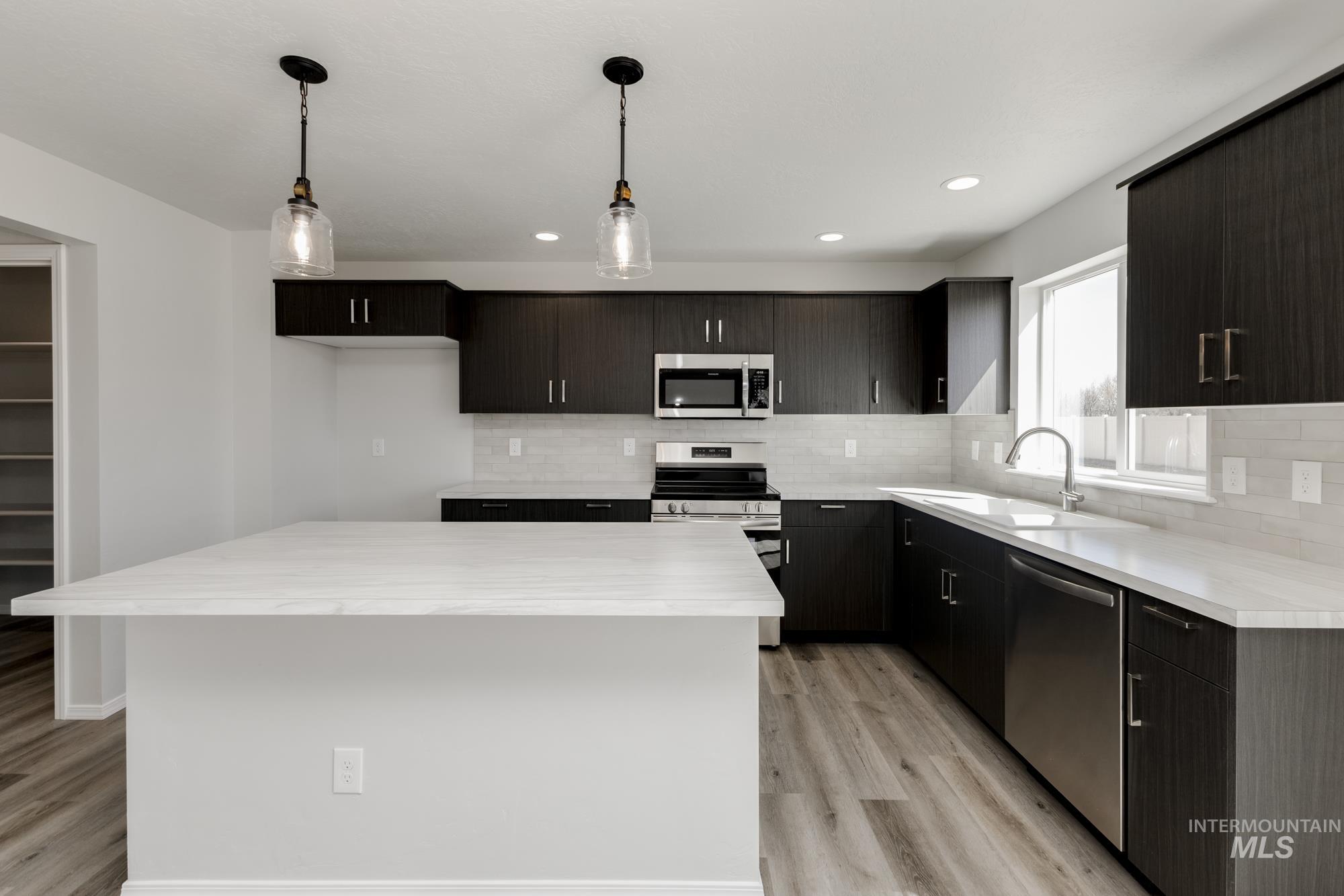 Kitchen featuring appliances with stainless steel finishes, hanging light fixtures, a center island, tasteful backsplash, and recessed lighting