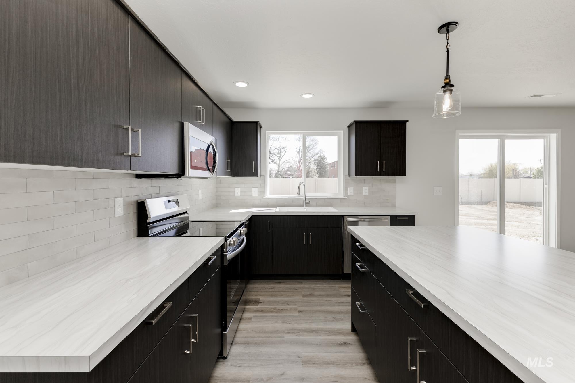 Kitchen with appliances with stainless steel finishes, dark cabinets, pendant lighting, light wood-style flooring, and tasteful backsplash