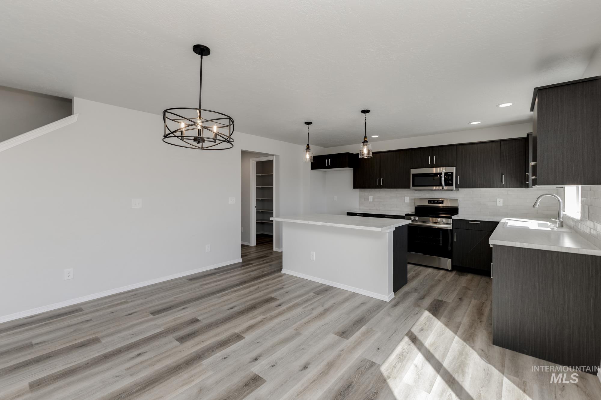 Kitchen with appliances with stainless steel finishes, dark cabinetry, a kitchen island, a chandelier, and pendant lighting